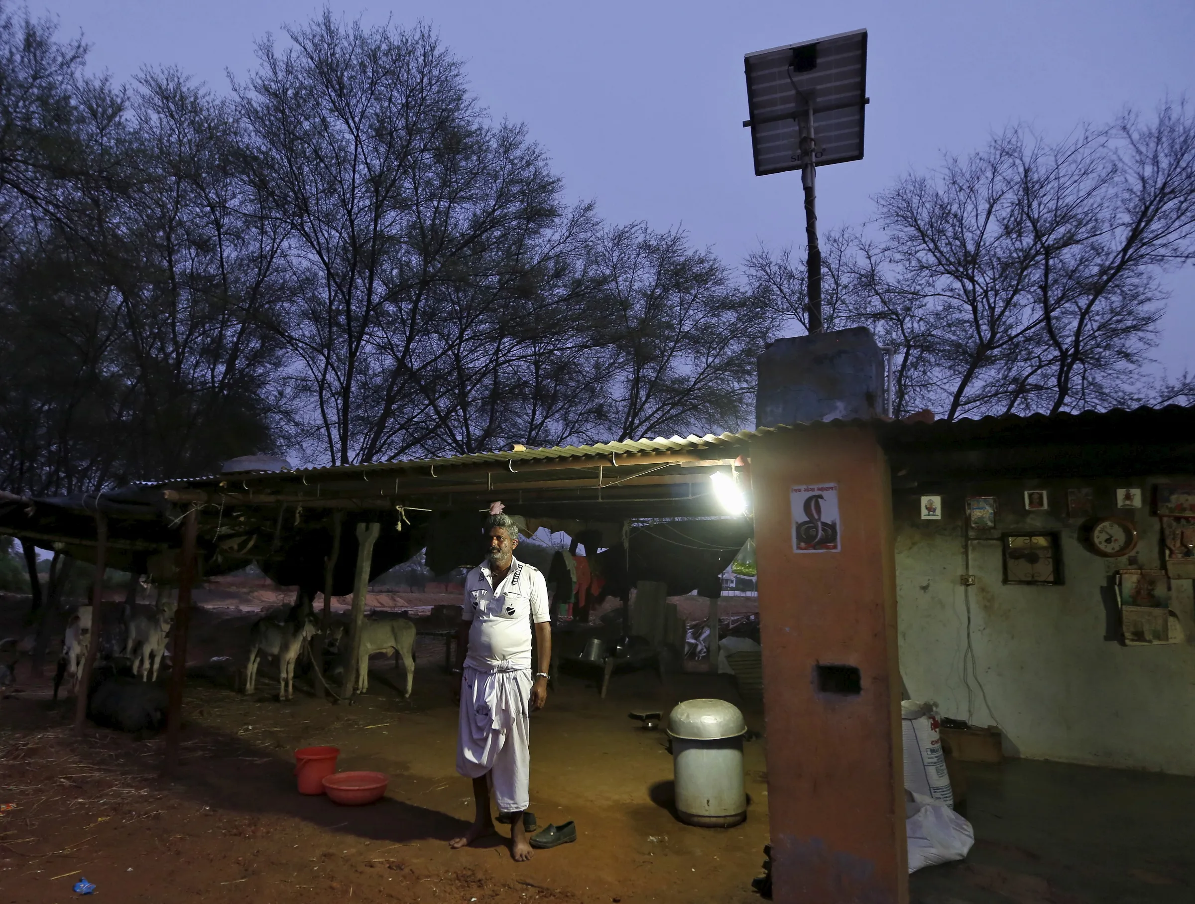 Villager Mohan Bharwad poses next to a Compact Fluorescent Lamp (CFL) powered by solar energy, outside his house on the outskirts of Gandhinagar, India, June 25, 2015