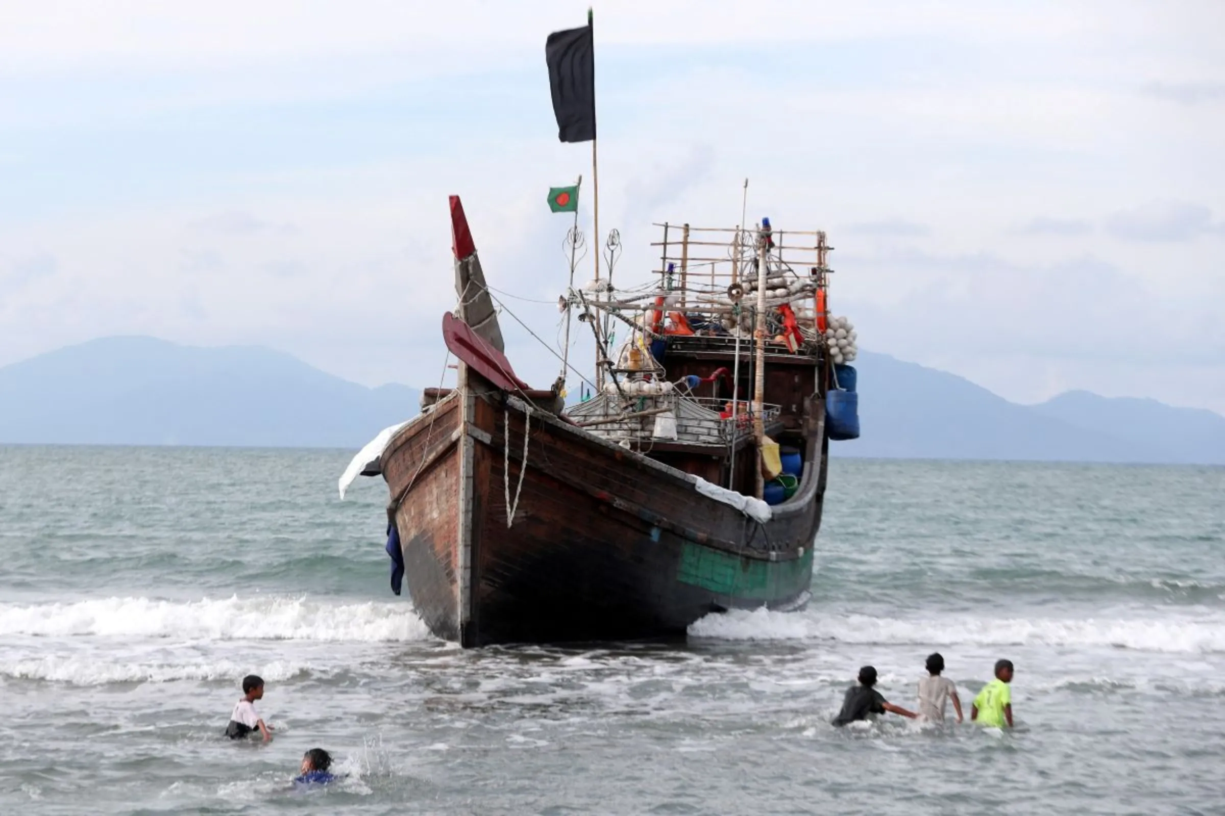 Children wade in the water near a wooden boat used to carry Rohingya refugees at Kuala Gigieng beach in Aceh Besar, Aceh province, Indonesia, January 8, 2023