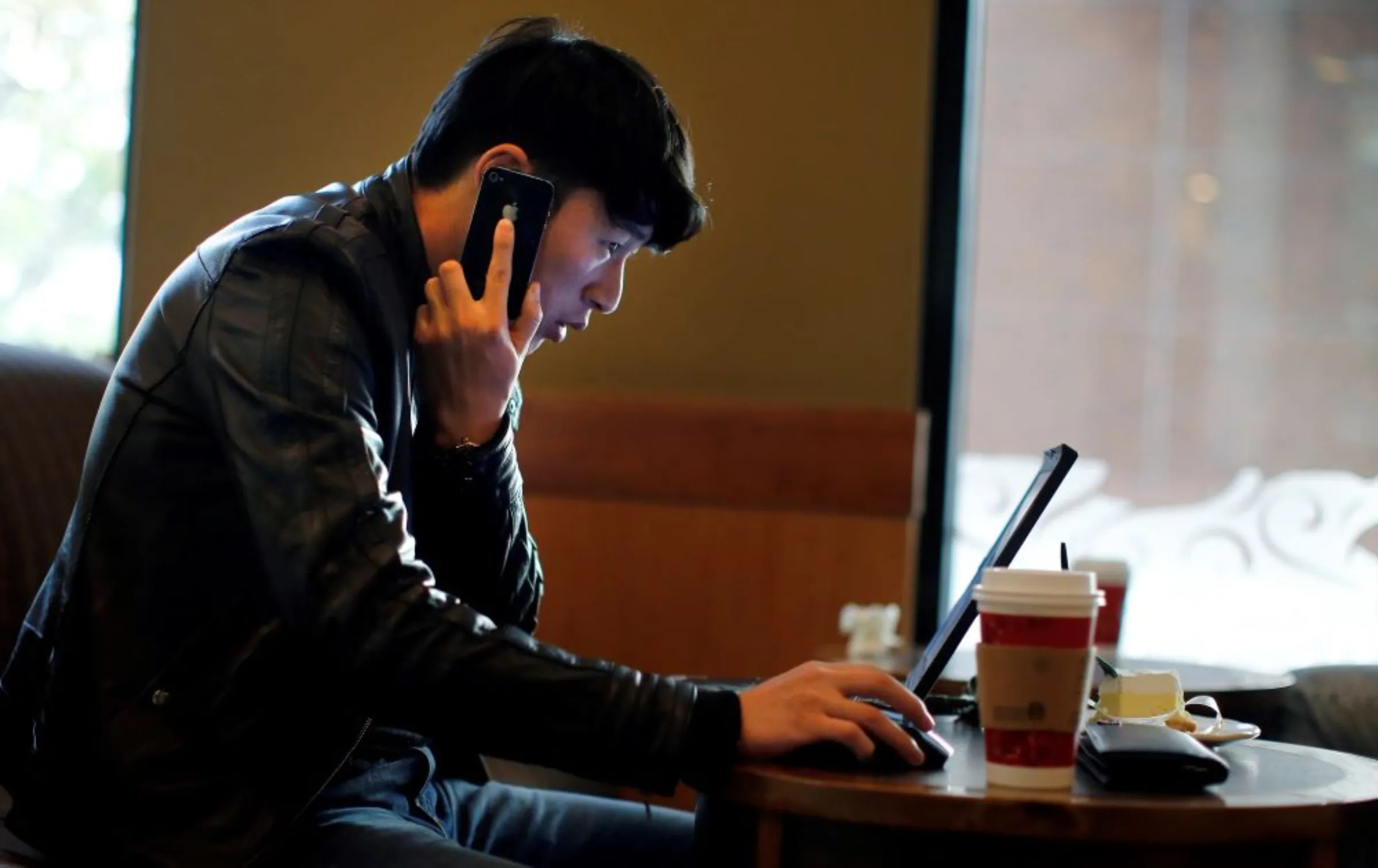 A man talks on the phone as he surfs the internet on his laptop at a local coffee shop in downtown Shanghai November 28, 2013. REUTERS/Carlos Barria