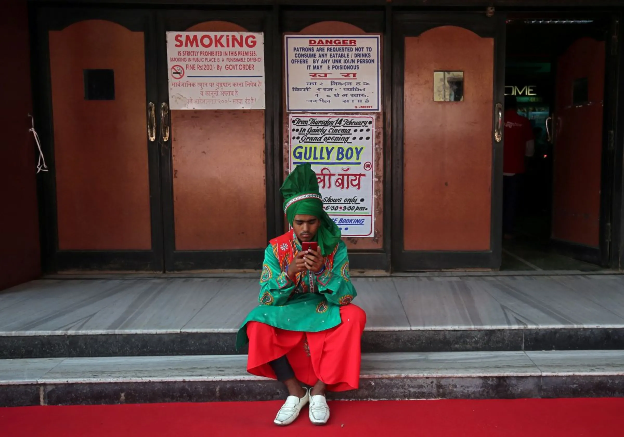 A man wearing traditional attire checks his mobile phone as he waits to perform before the launch of the trailer of a Bollywood movie outside a cinema in Mumbai, India, February 20, 2019. REUTERS/Francis Mascarenhas