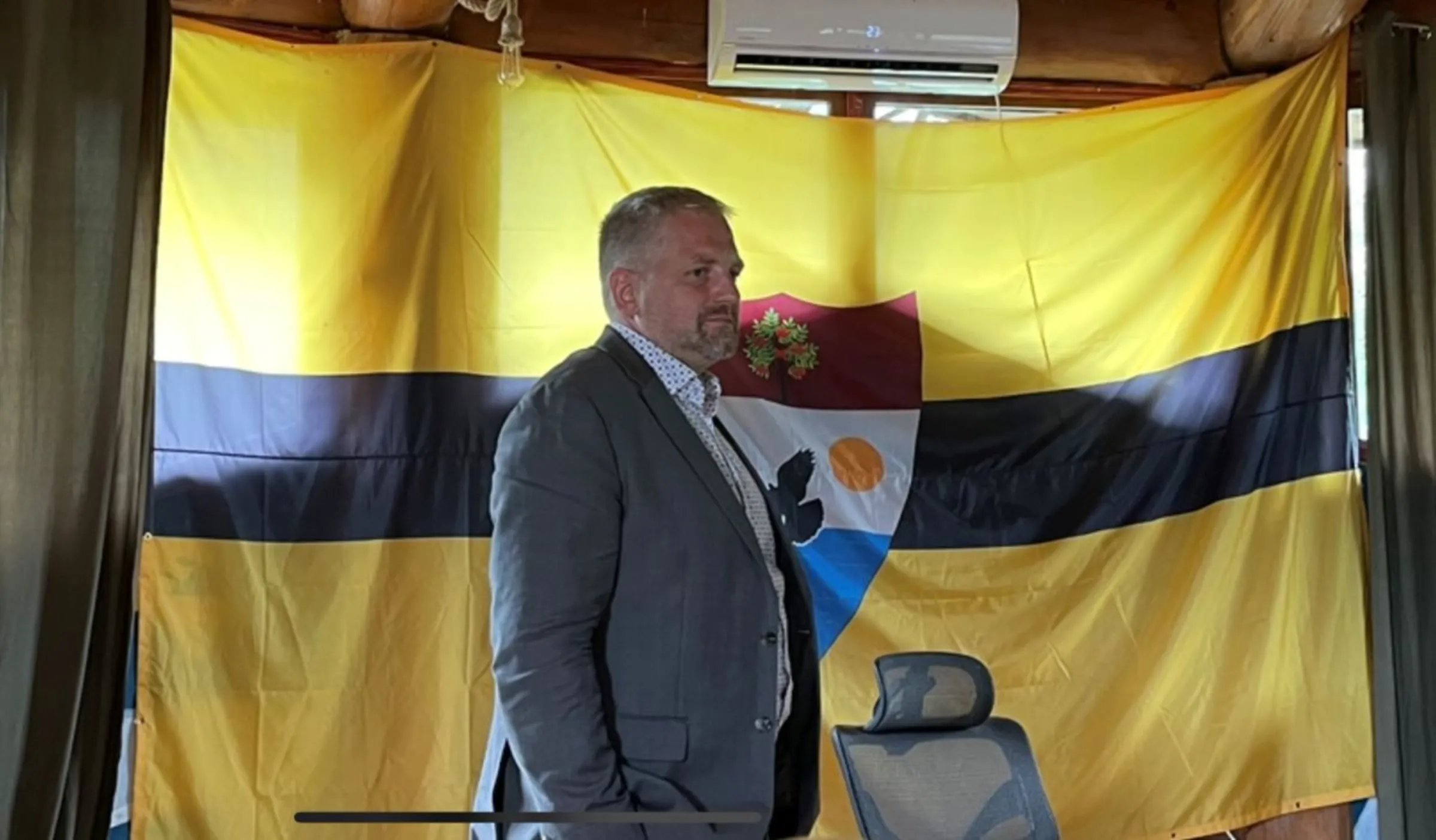 Vít Jedlička, the right-libertarian president of Liberland, standing in front of the nation's flag at the Floating Man festival. August 6 2023. Thomson Reuters Foundation/Adam Smith