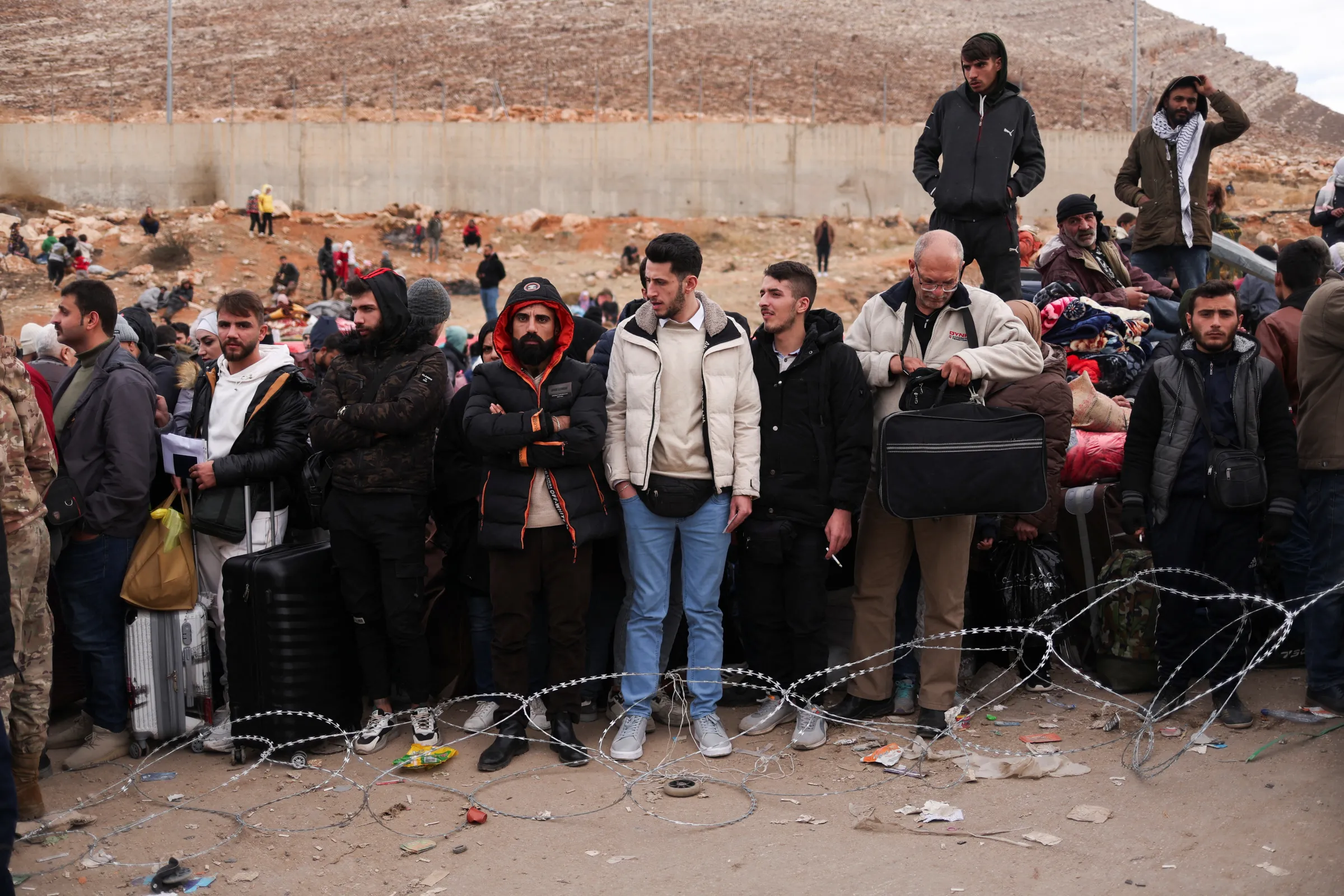 People line up behind a razor wire fence while waiting to cross the Lebanese border, at the Masnaa Border Crossing, Syria, December 12, 2024. REUTERS/Amr Alfiky