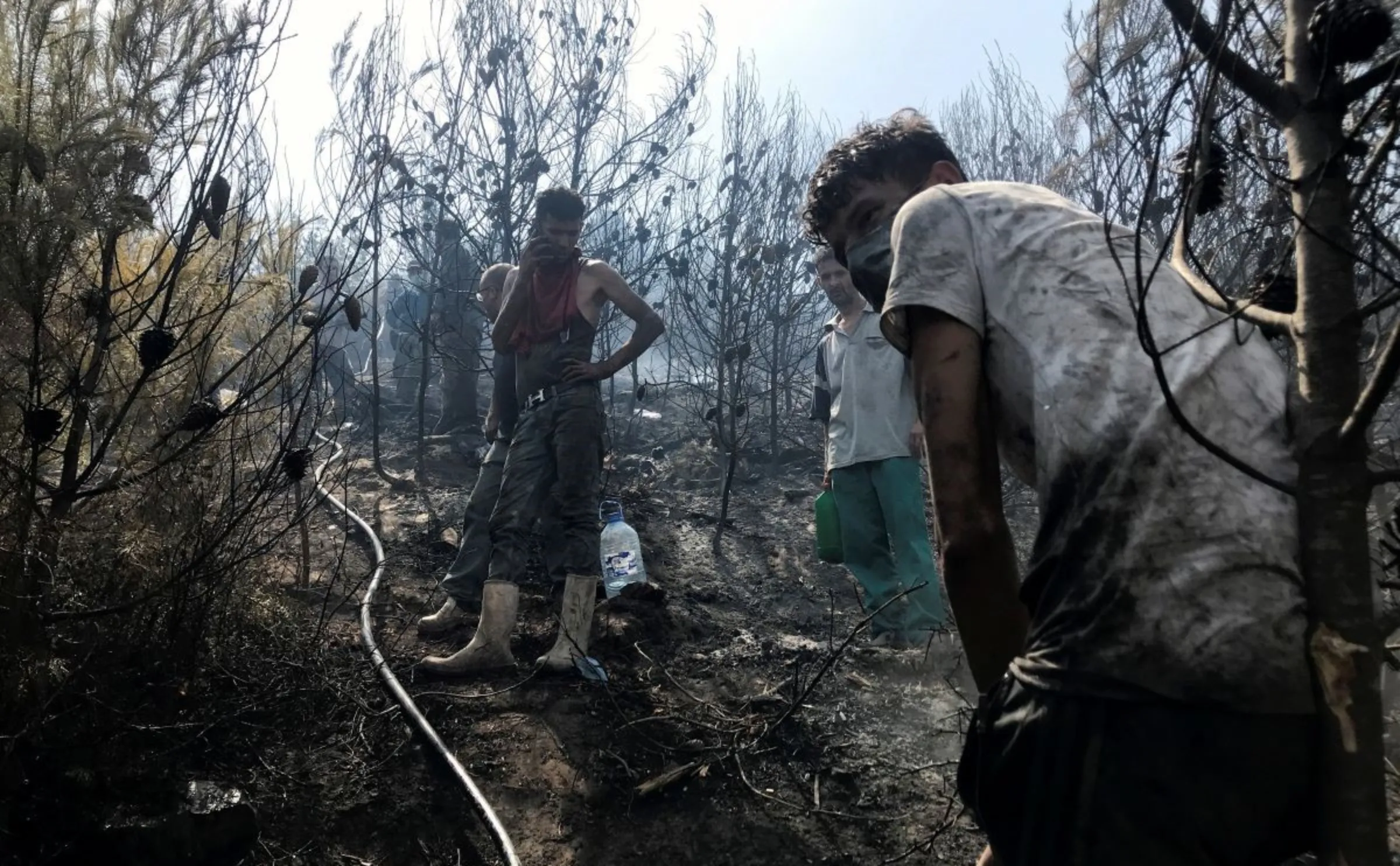 Men work to douse hotspots in an area hit by a wildfire in El Bir village, Bejaia province, Algeria August 16, 2021. REUTERS/Abdelaziz Boumzar