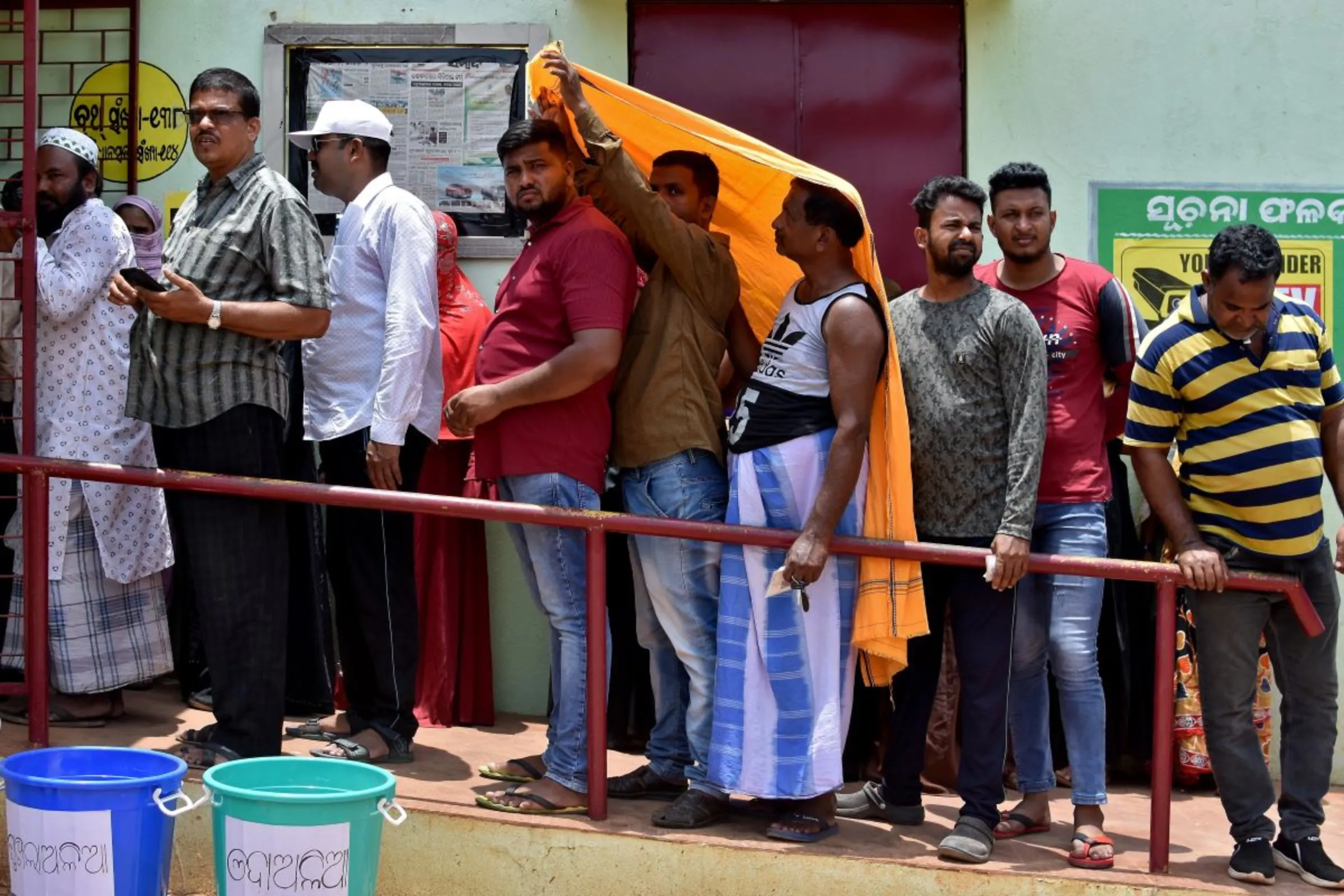 Men use a stole to cover from heat as they wait in a line outside a polling station to cast their votes during the sixth phase of India's general election, on a hot summer day in Bhubaneswar, India, May 25, 2024. REUTERS/Stringer
