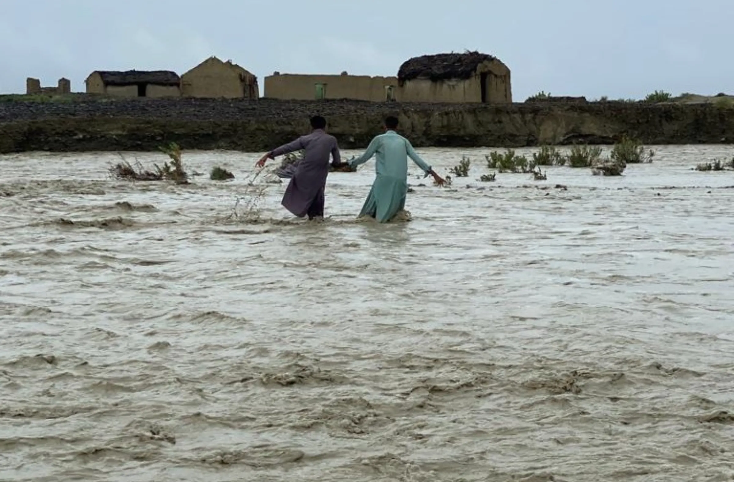 Two men cross floodwaters in Awaran district, in Balochistan province, September 1, 2022. Thomson Reuters Foundation/Dilshad Baloch