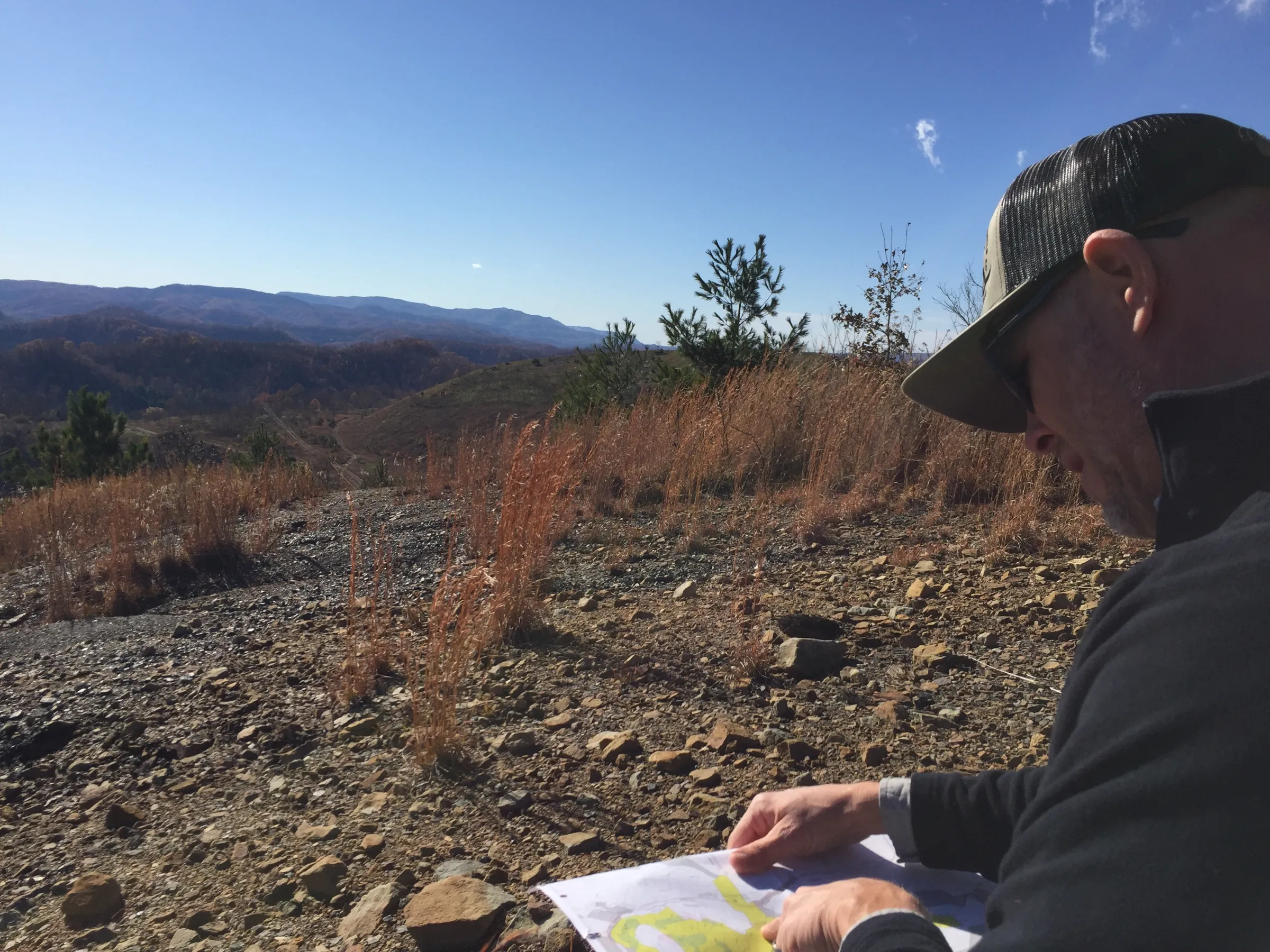 A man looks at a map sat on rocky ground