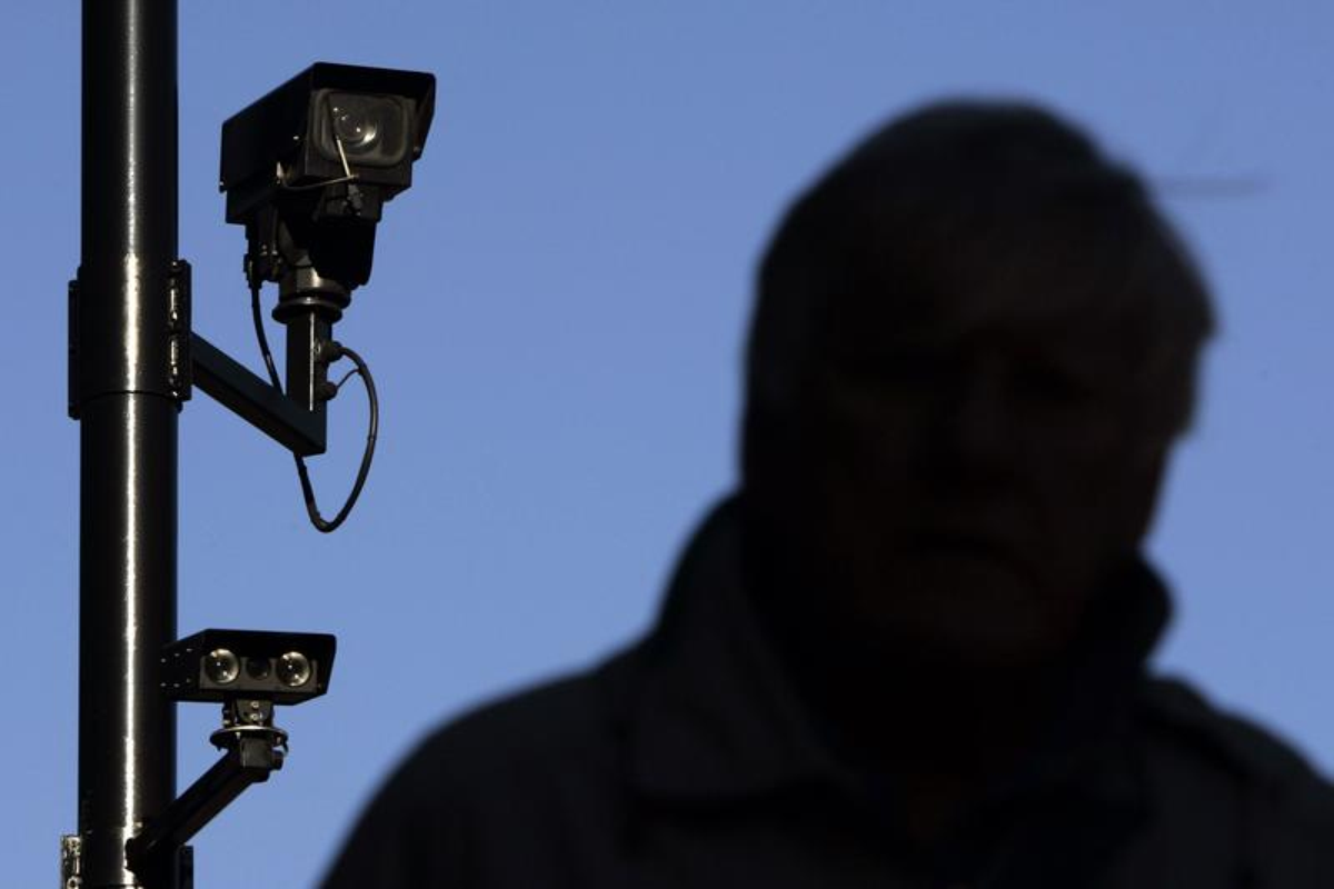 A security camera overlooks a man as he walks down a street in London November 2, 2006. REUTERS/Luke MacGregor