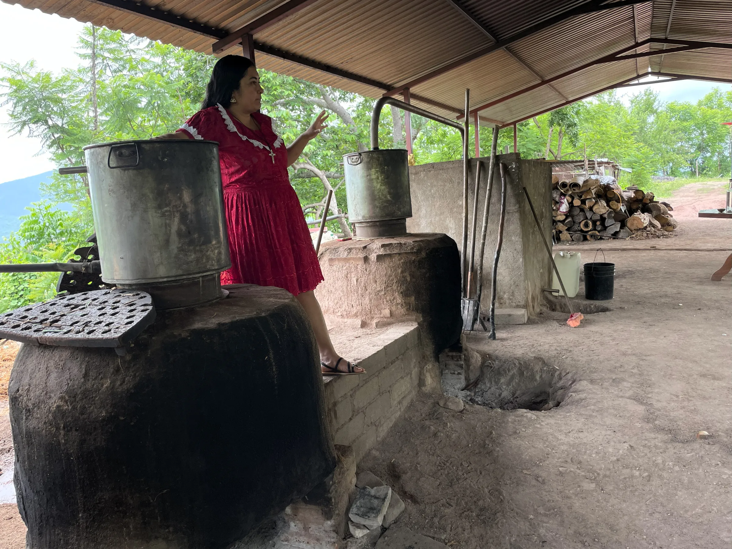Mezcal producer Oliva Ramírez stands between two ovens where mezcal is distilled at a local palenque in Sola de Vega, Oaxaca, Mexico. June 24, 2025. . Thomson Reuters Foundation/Diana Baptista