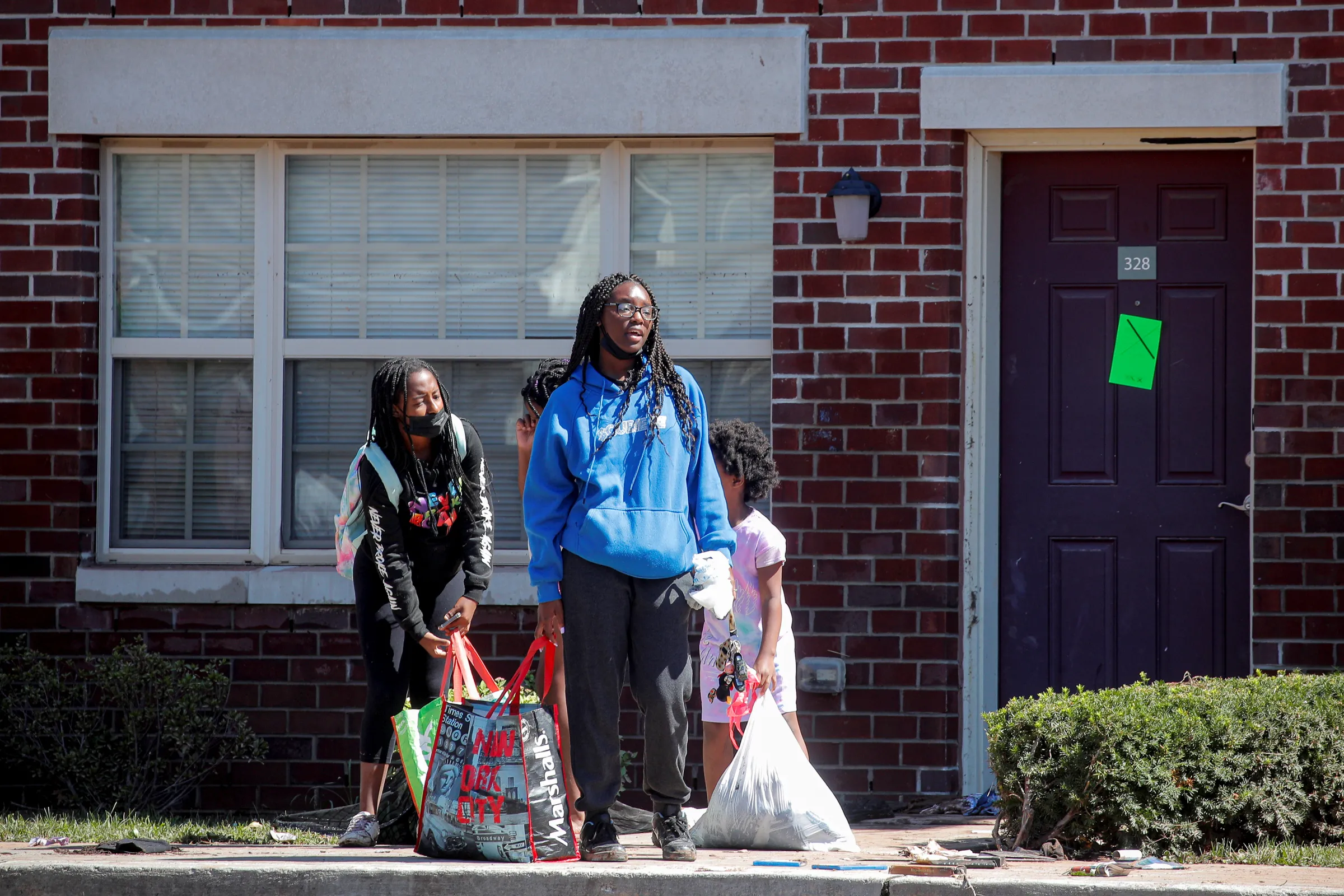 Three children hold bags as they stand in front of a house