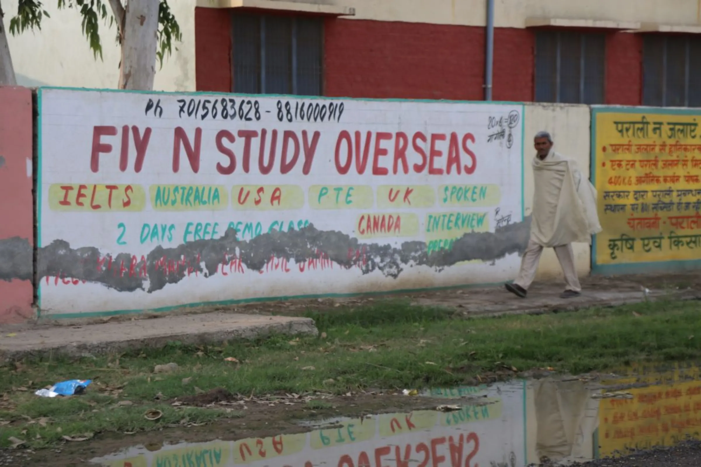 A man walks by a painted advertisement for overseas study in Madlauda, India, December 4, 2023. Thomson Reuters Foundation/Annie Banerji