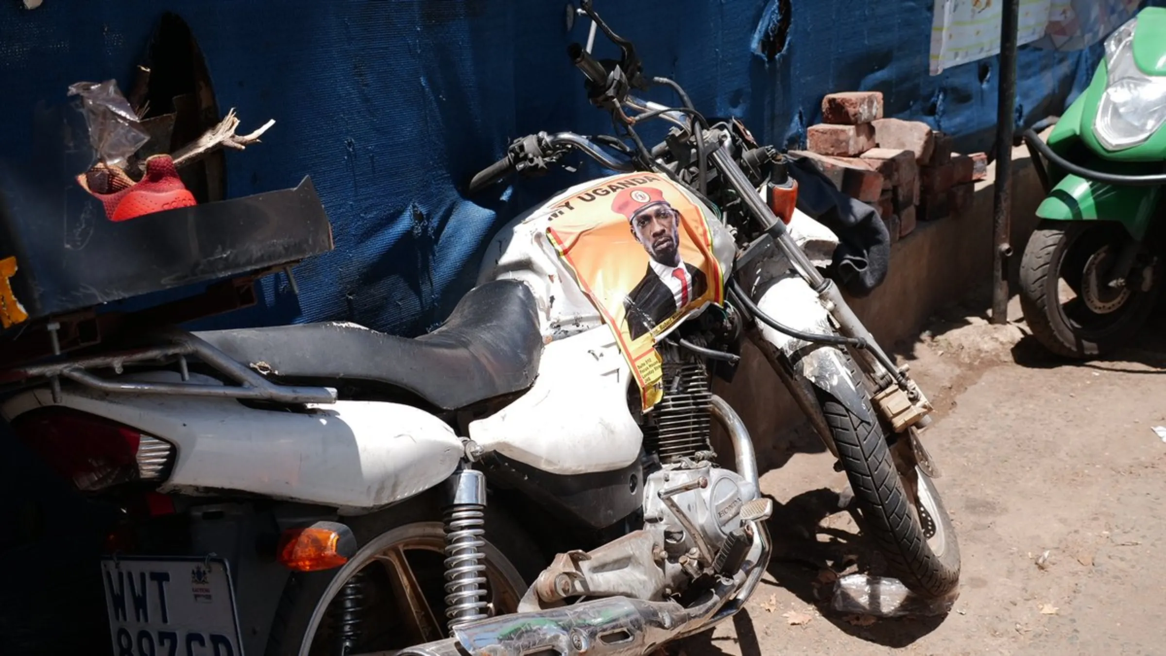 A damaged food delivery motorcycle with a poster of Bobi Wine, a Ugandan singer and politician, leans against a wall in Johannesburg, South Africa. January 22, 2021. Thomson Reuters Foundation/Kim Harrisberg