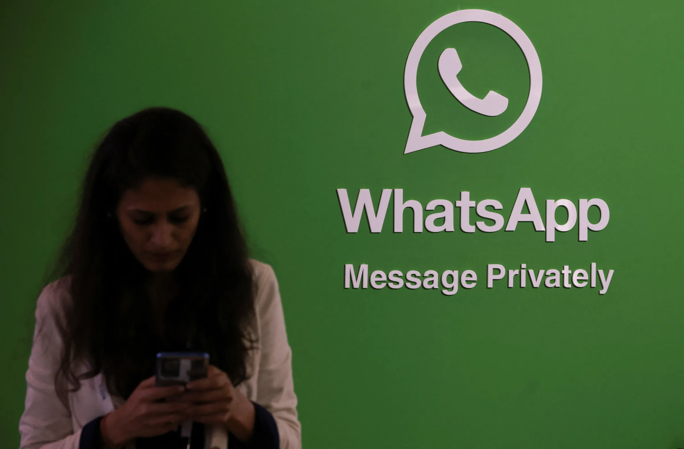 A woman uses her phone next to a logo of the WhatsApp application during Global Fintech Fest in Mumbai, India September 20, 2022