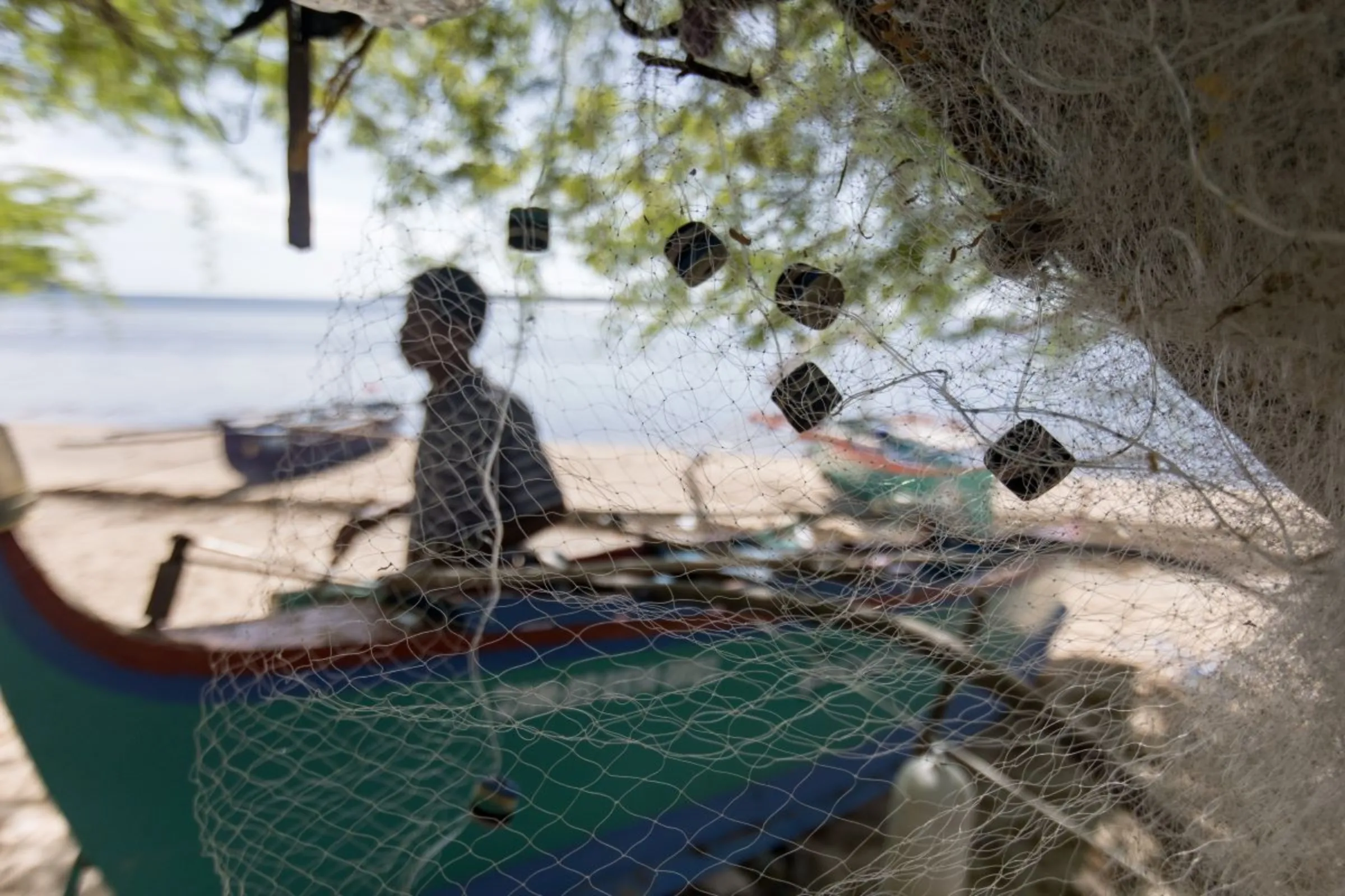 A fisherman stands in silhouette behind a boat on San Salvador Island, Masinloc in Zambales Province in the Philippines. Fishermen on the island say China’s attempts to block them from fishing at the Scarborough Shoal is costing them money and threatening their livelihoods. Nov. 16, 2023. Thomson Reuters Foundation/Kathleen Limayo