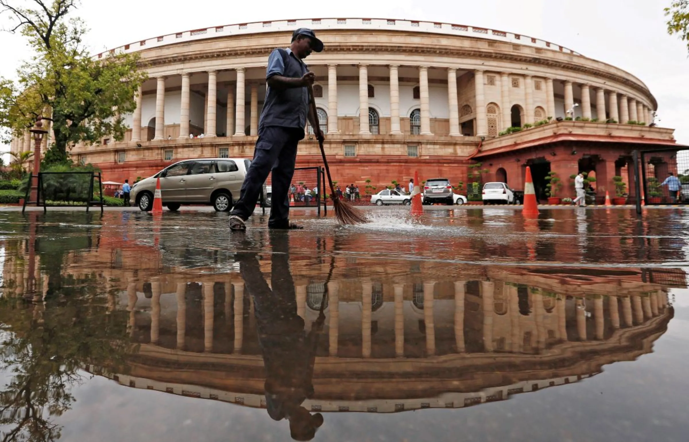 Indian parliament building is reflected in a puddle after the rain as a man sweeps the water in New Delhi, India July 20, 2018. REUTERS/Adnan Abidi
