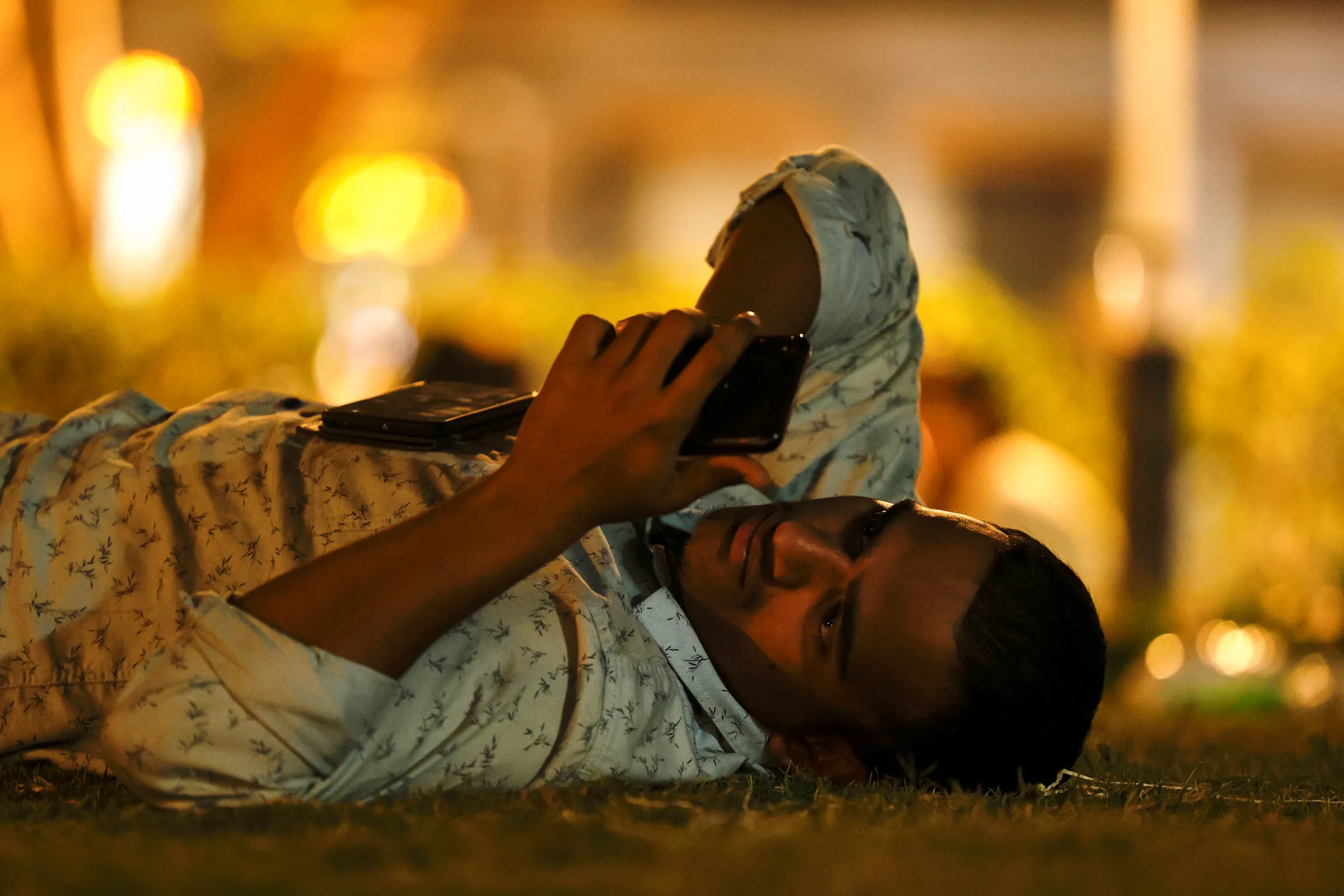 A man uses his mobile phone while lying in a park in New Delhi, India, March 27, 2025. REUTERS/Priyanshu Singh