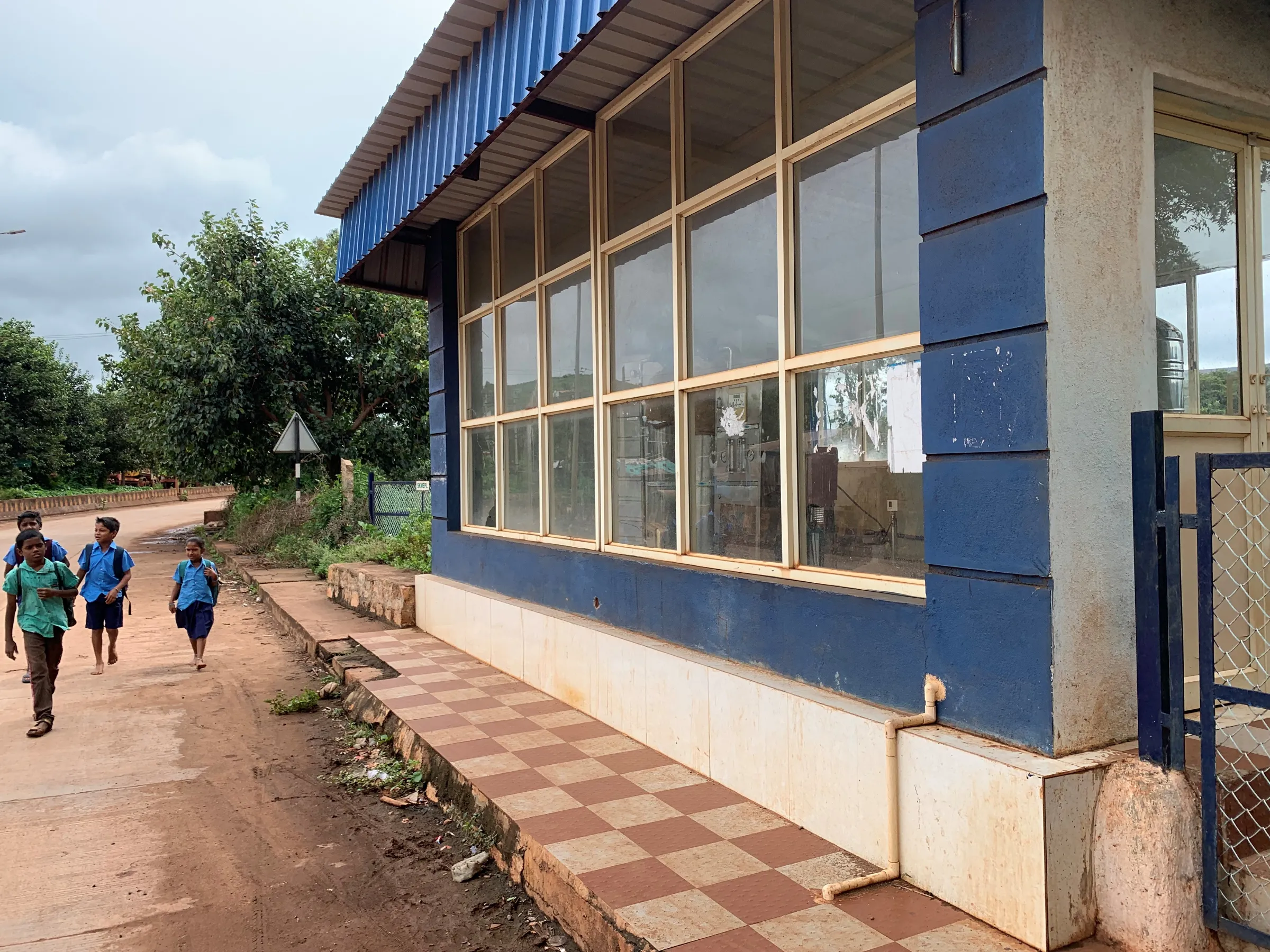 A building with blue walls and lots of windows next to a dirt road, where children walk