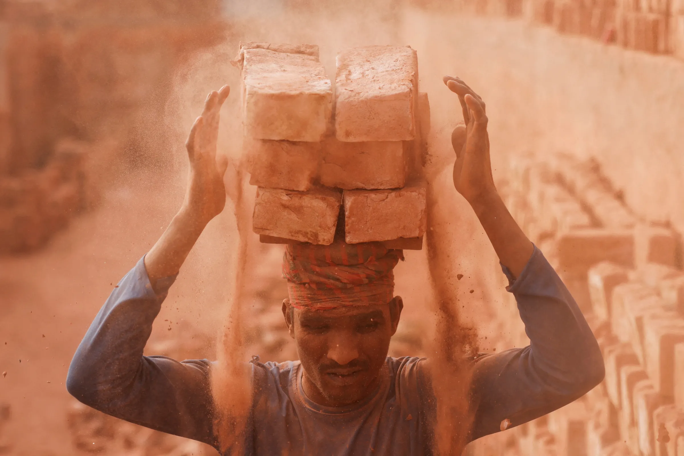 A worker loads bricks on his head in the dusty working environment of a brick factory, as he transports them to another place, in Dhaka, Bangladesh, January 16, 2024. REUTERS/Mohammad Ponir Hossain
