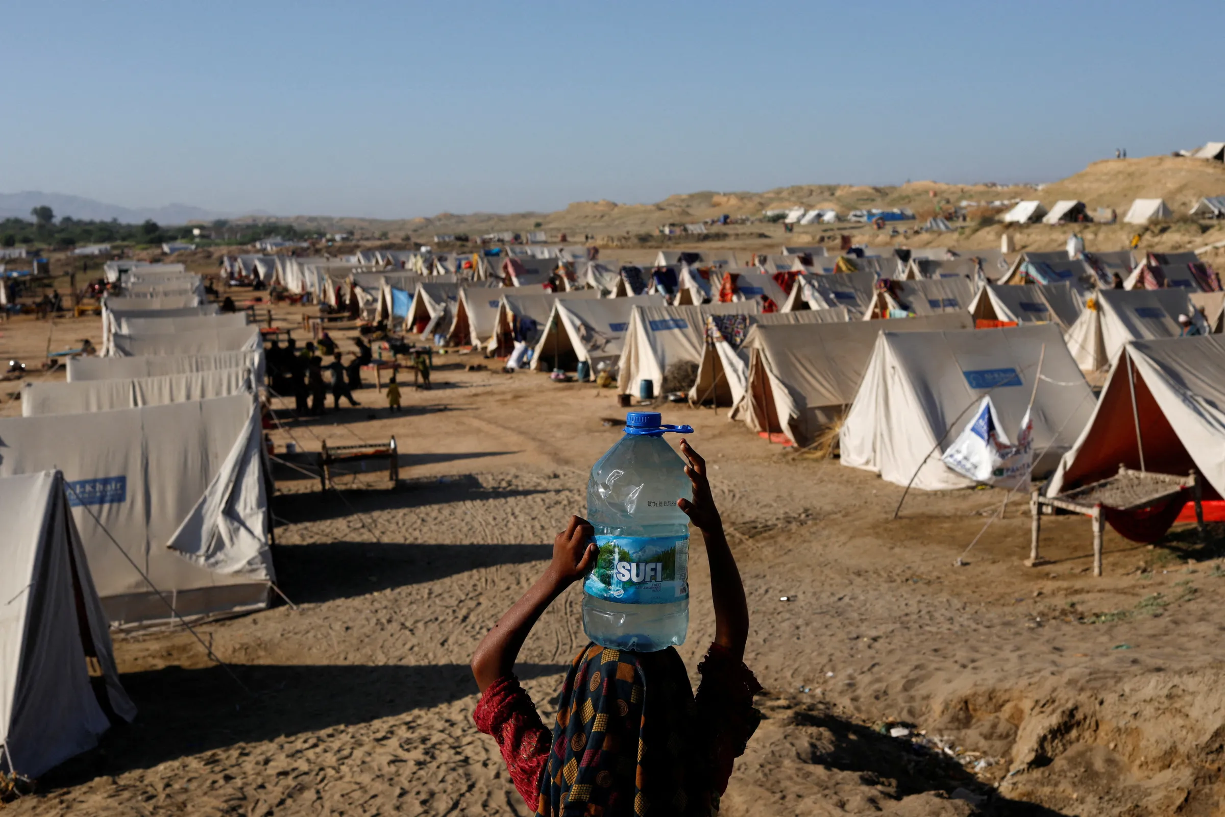 A displaced girl carries a bottle of water she filled from nearby stranded flood-waters, as her family takes refuge in a camp, in Sehwan, Pakistan, September 30, 2022. REUTERS/Akhtar Soomr