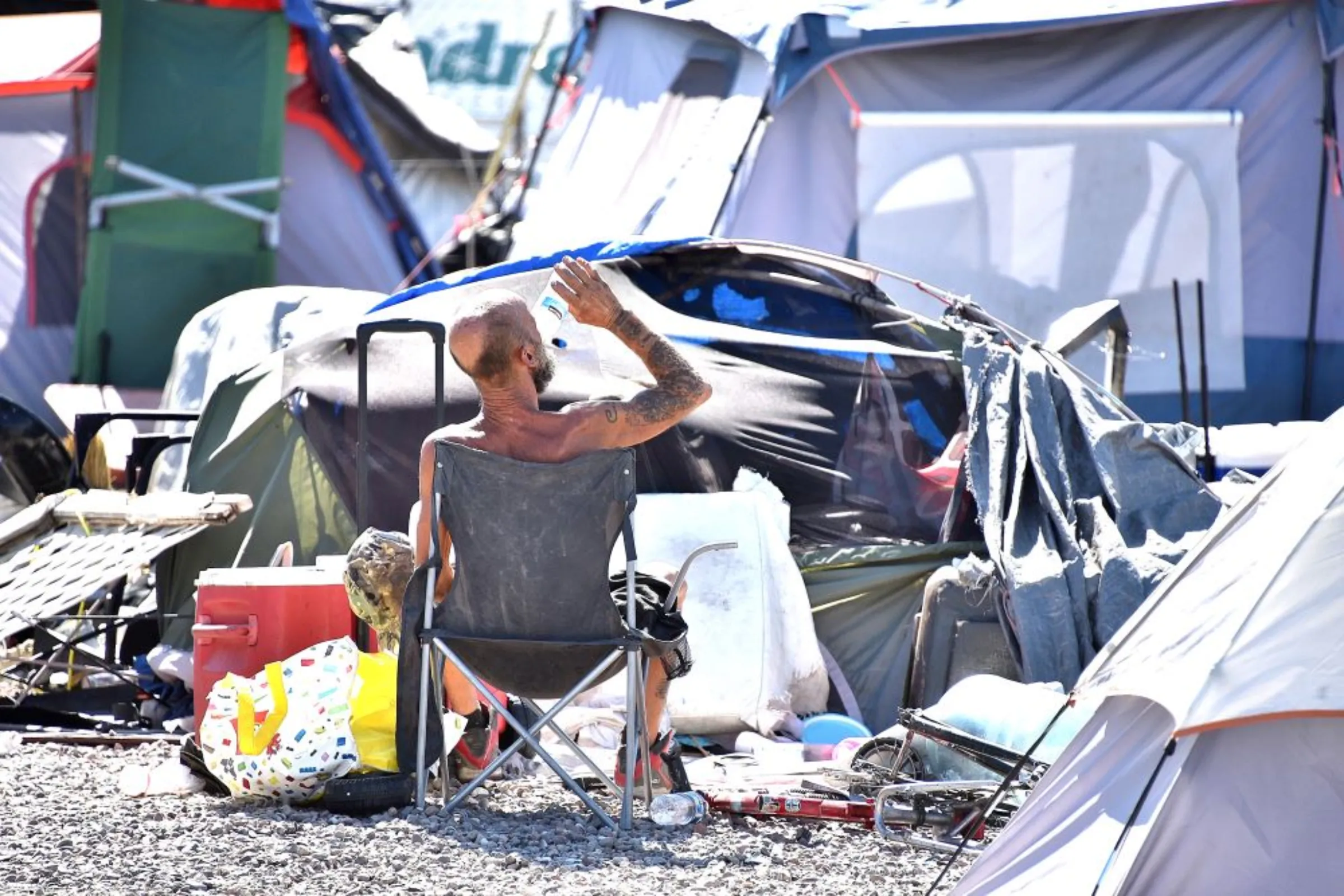 A man drinks from a bottle of water as he sits on a camping chair surrounded by suitcases and tents in a camp for those experiencing homelessness on county land in Phoenix, Arizona. Steve Carr/Human Services Campus/Handout via Thomson Reuters Foundation