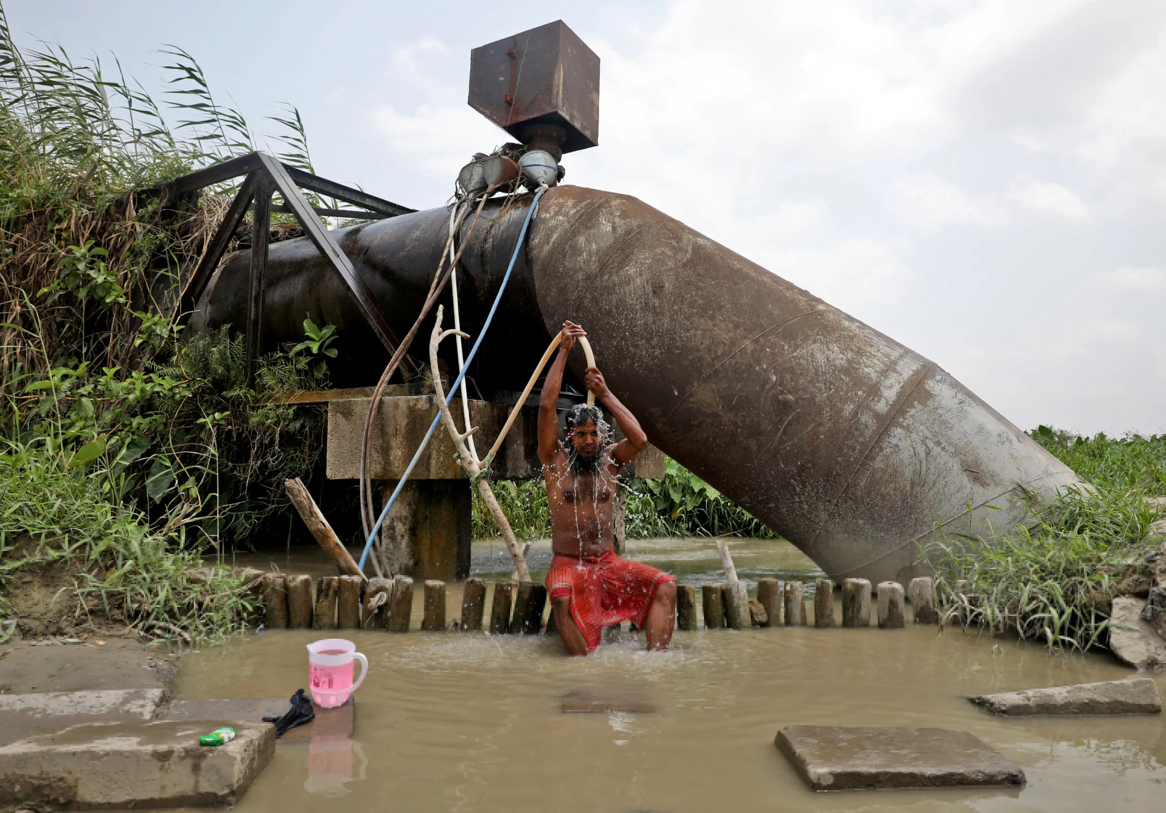 A man bathes with a pipe connected to the valve of a water supply pipe