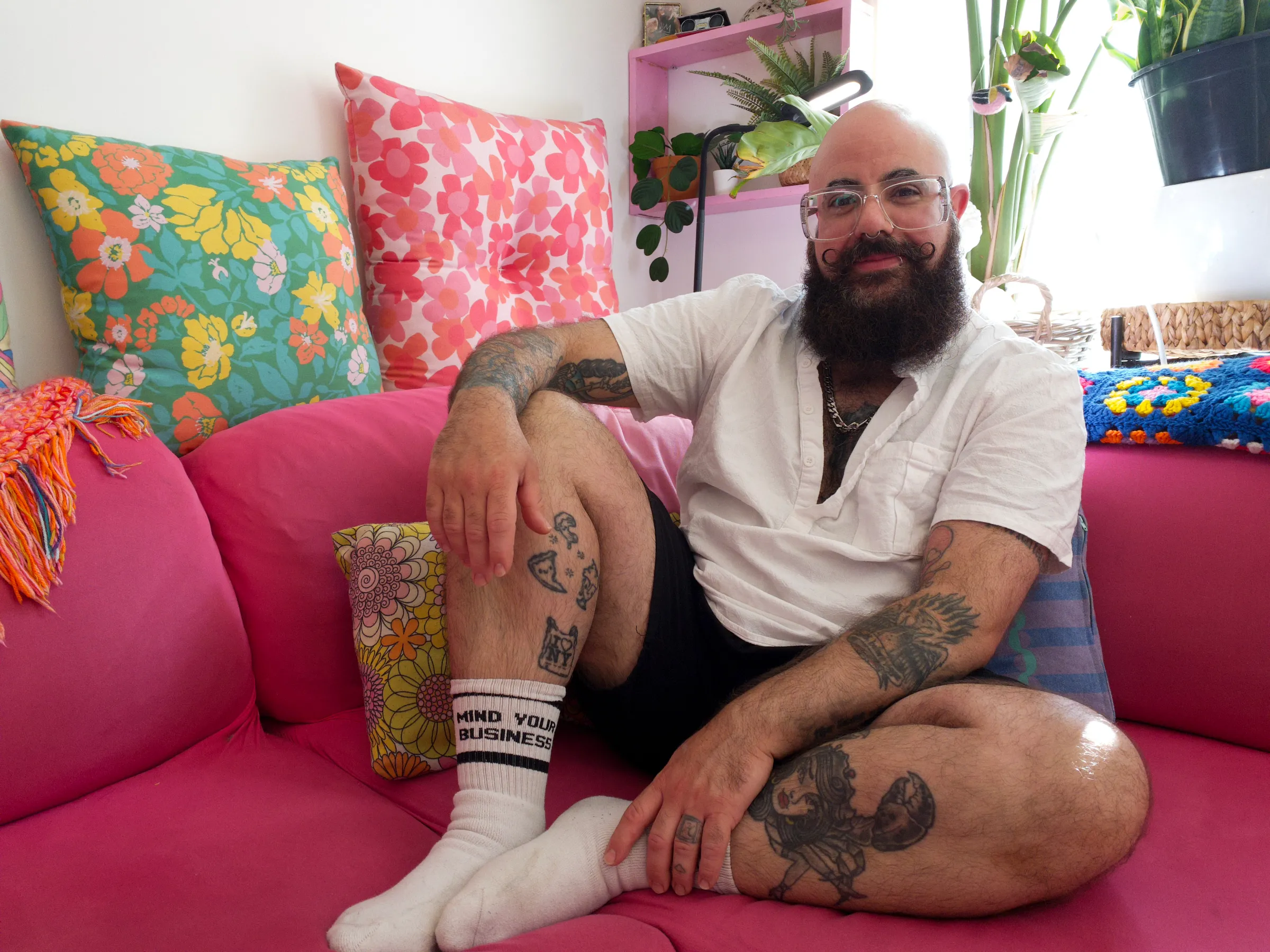 In the vibrantly coloured living room of his Amsterdam West flat, Topher Gross sits on the pink couch he and his partner chose together, 10 July 2025. Ingrid Gercama/