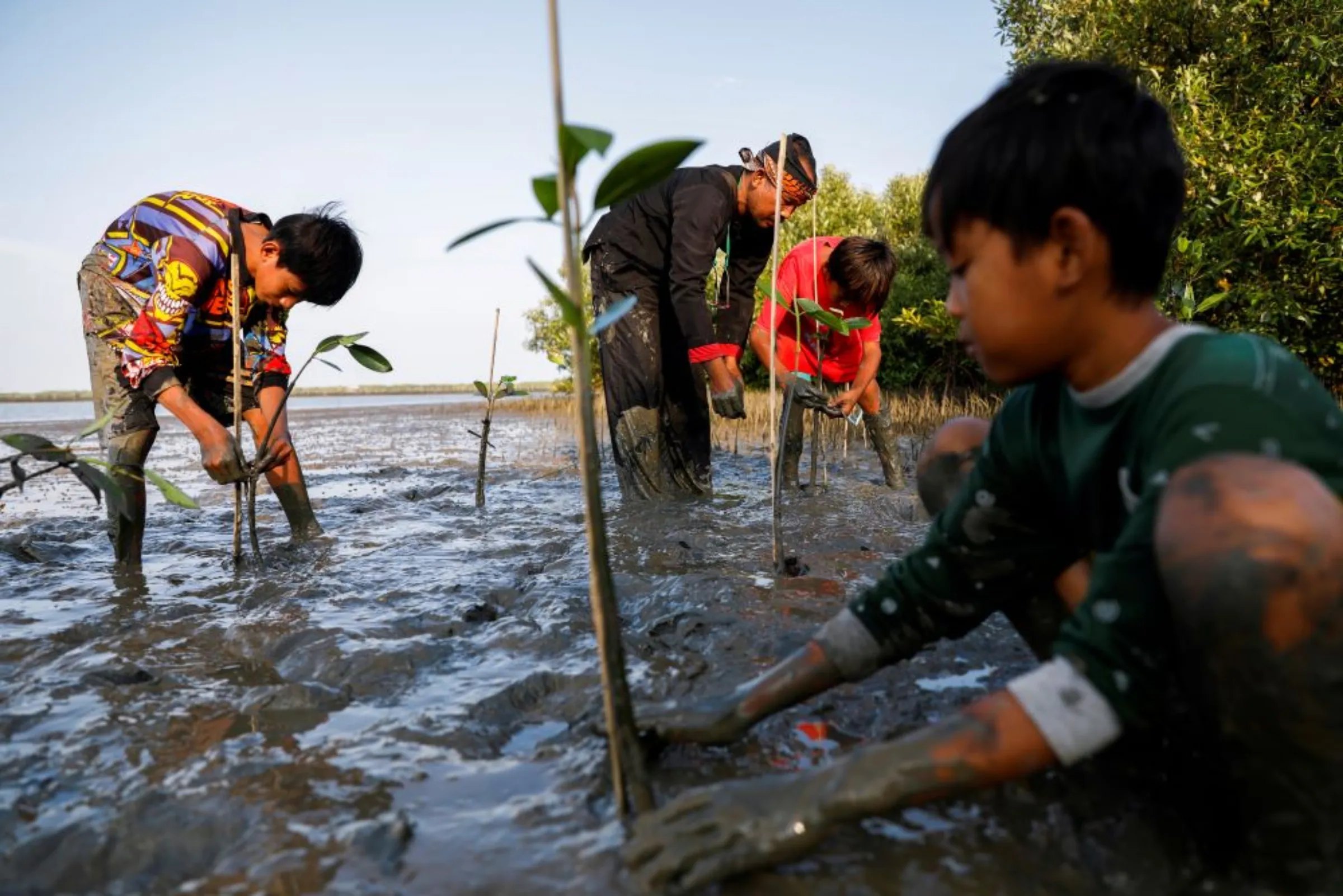 A man plants mangrove trees with local children at Tiris beach in Pabeanilir village, Indramayu regency, West Java province, Indonesia, March 11, 2021. Picture taken March 11, 2021. REUTERS/Willy Kurniawan
