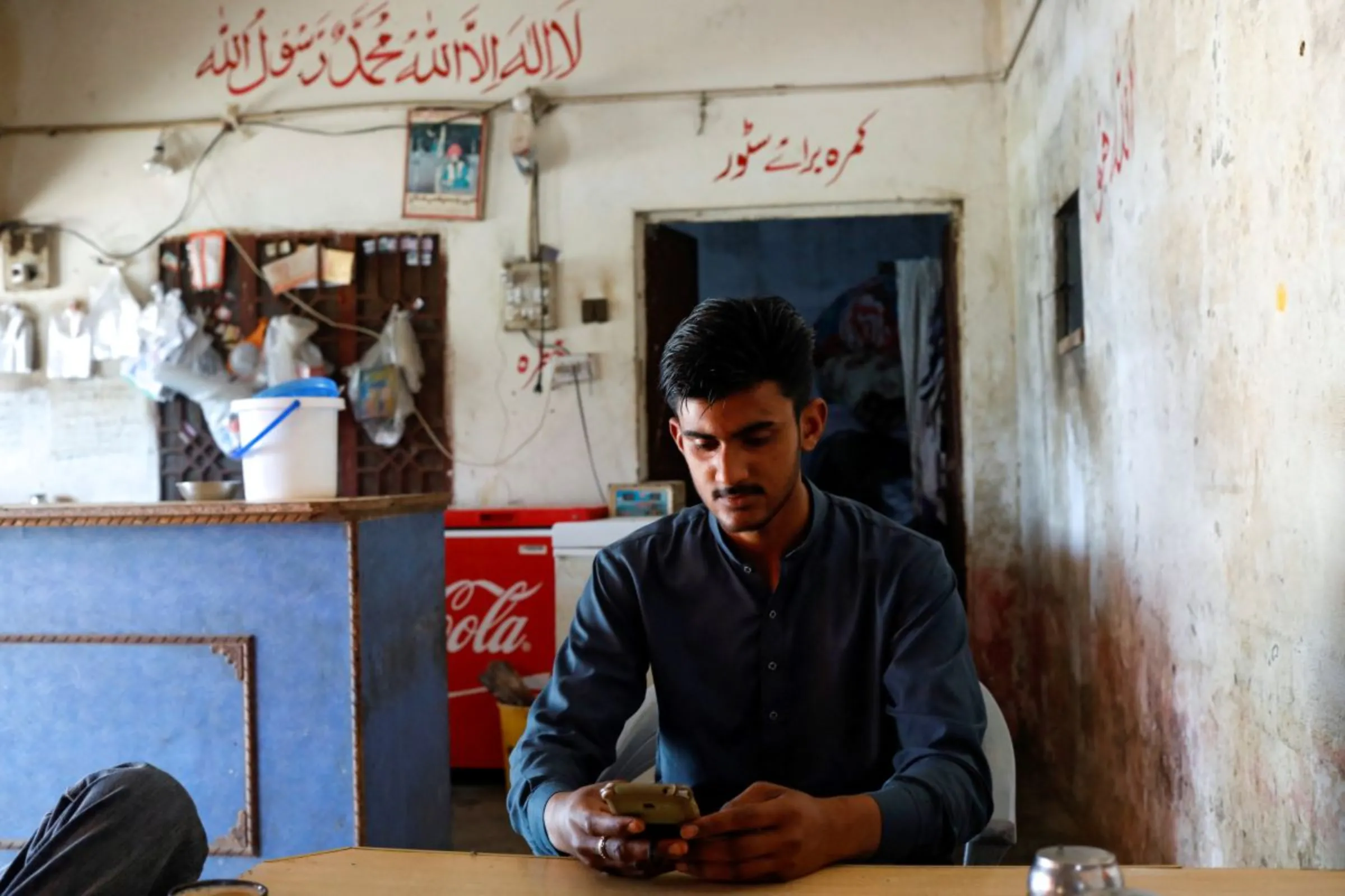 A man looks at pictures on a mobile phone, at a tea stall in Bhojpur town in Gujrat district of Punjab province, Pakistan March 7, 2023