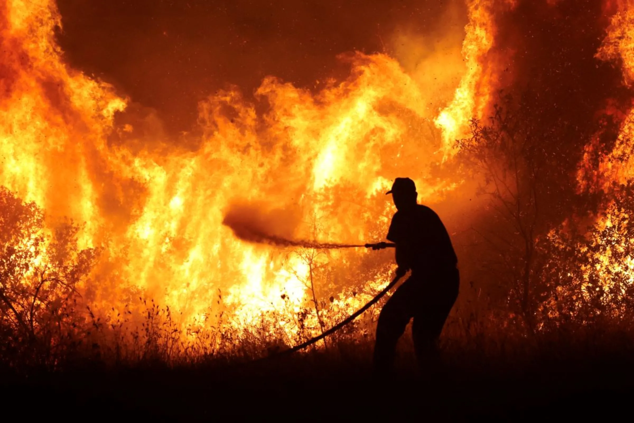 A firefighter tries to extinguish a wildfire burning at the industrial zone of the city of Volos in central Greece, July 26, 2023. REUTERS/Alexandros Avramidis