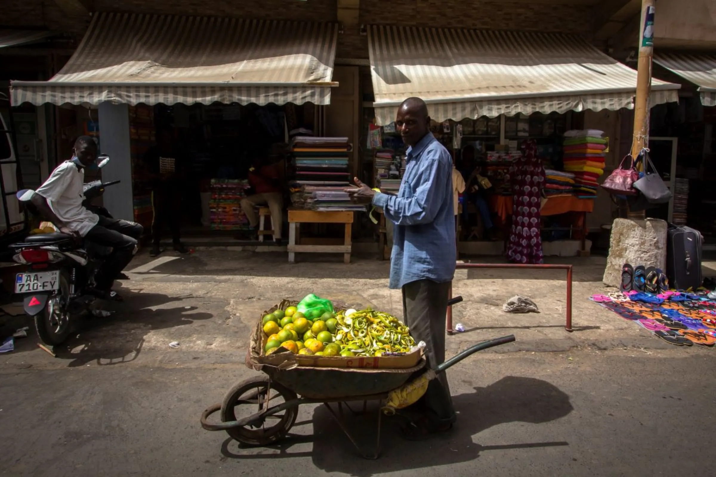 Mobile vendor Souleymane Ba looks at the camera while peeling oranges he is selling from a wheelbarrow in Sandaga Market, Avenue Lamine Gueye, Dakar, Senegal, February 10, 2022. Marta Moreiras for StreetNet/Handout via Thomson Reuters Foundation