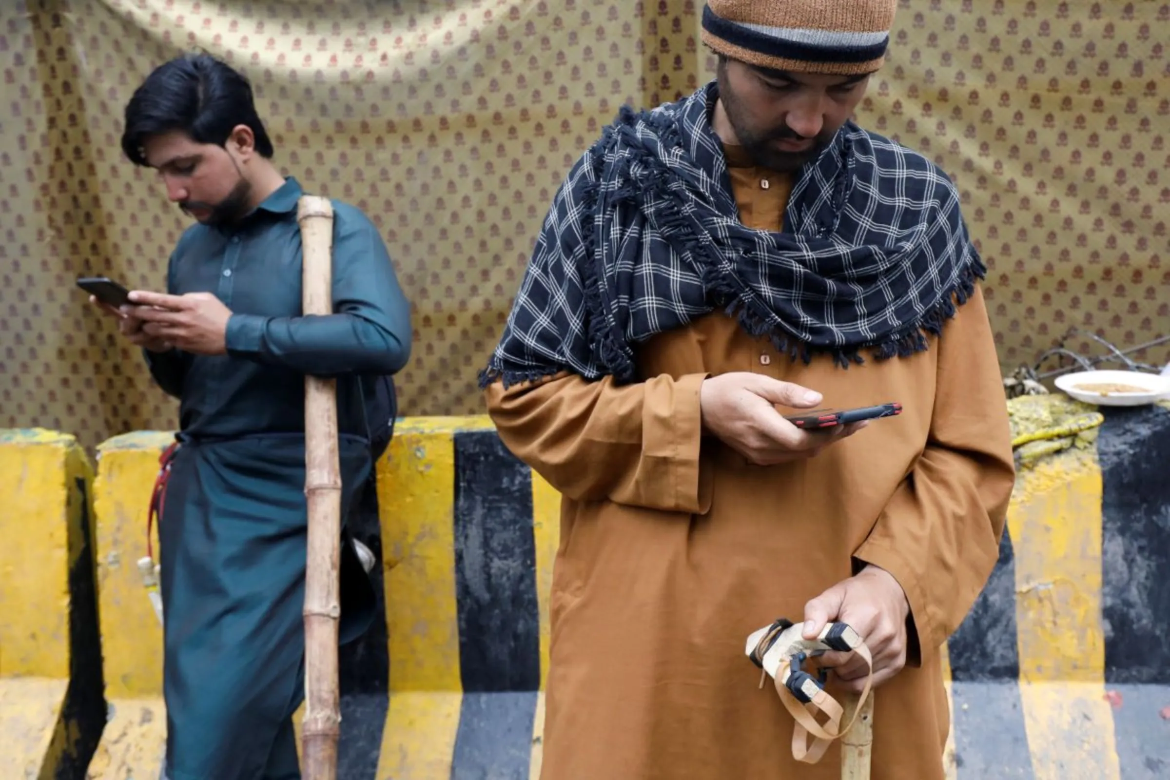 Supporters of former Pakistani Prime Minister Imran Khan, carrying a bamboo stick and a slingshot, use their mobile phones as they guard the entrance of Khan's house, in Lahore, Pakistan March 17, 2023. REUTERS/Akhtar Soomro