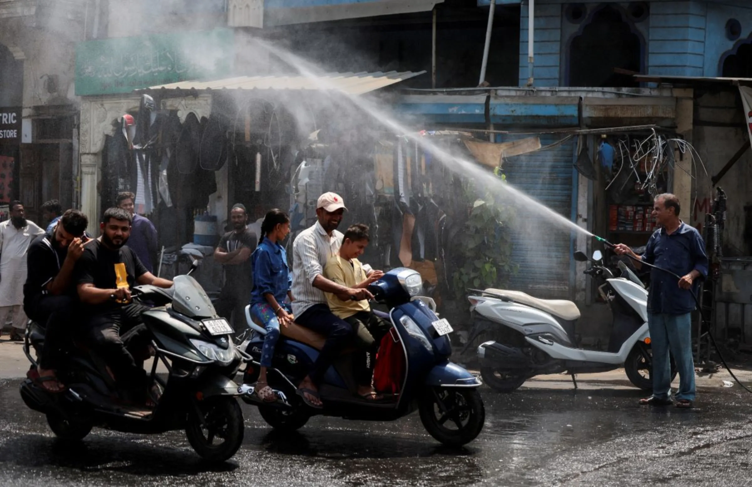 People on their scooters pass under a water sprinkler on a hot summer day in Ahmedabad, India, May 9, 2024. REUTERS/Amit Dave