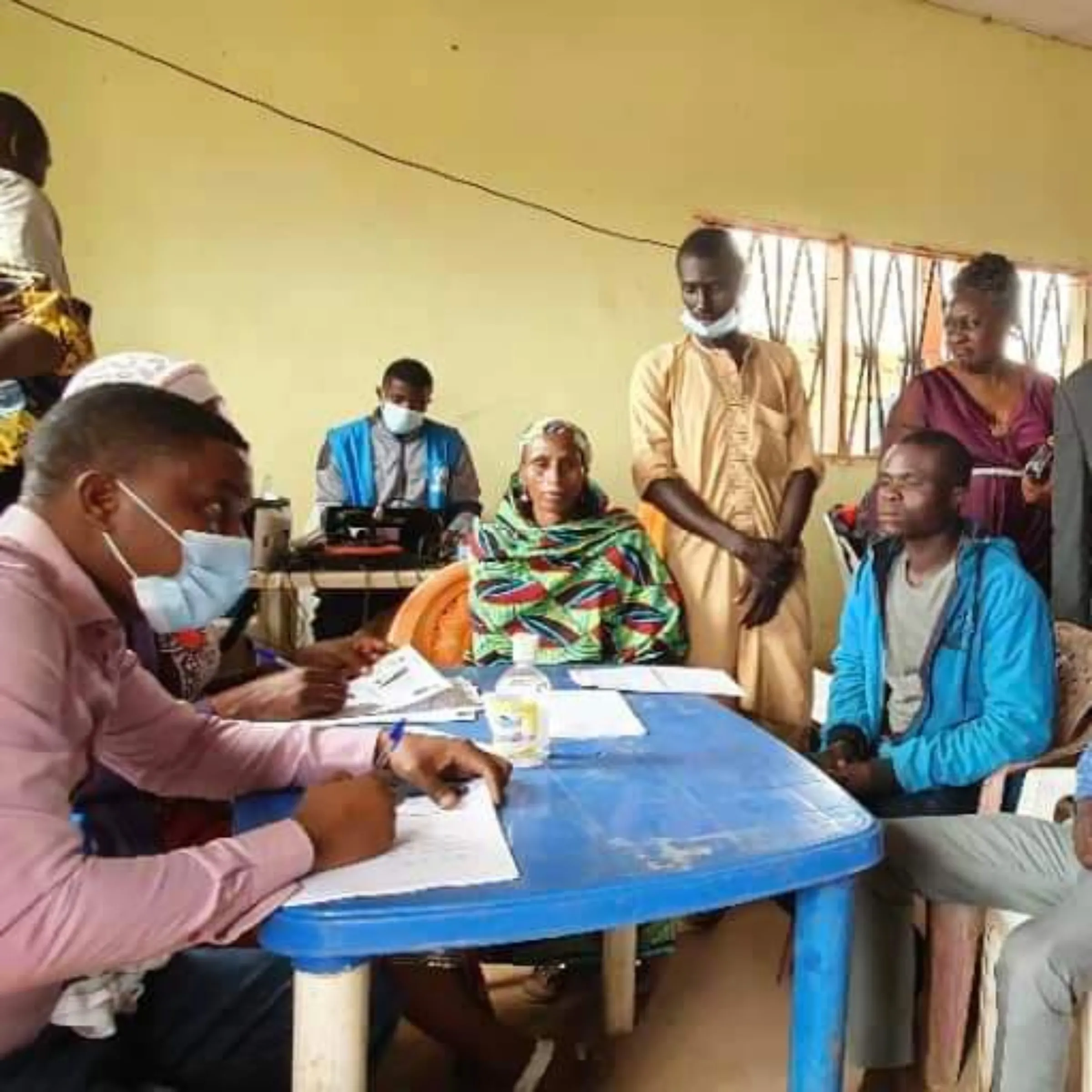 Refugees from the Central African Republic wait as an official signs papers on a blue plastic table to get their digital IDs at a camp in Cameroon.