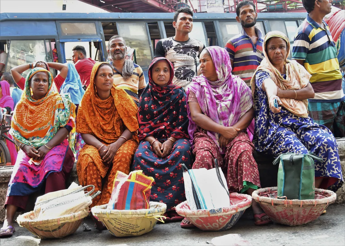 Construction worker Moina Begum (in gold clothing), sit with other day labourers waiting unsuccessfully for work near the Mirpur bridge in Dhaka, Bangladesh, August 16, 2022. Thomson Reuters Foundation/Mosabber Hossain