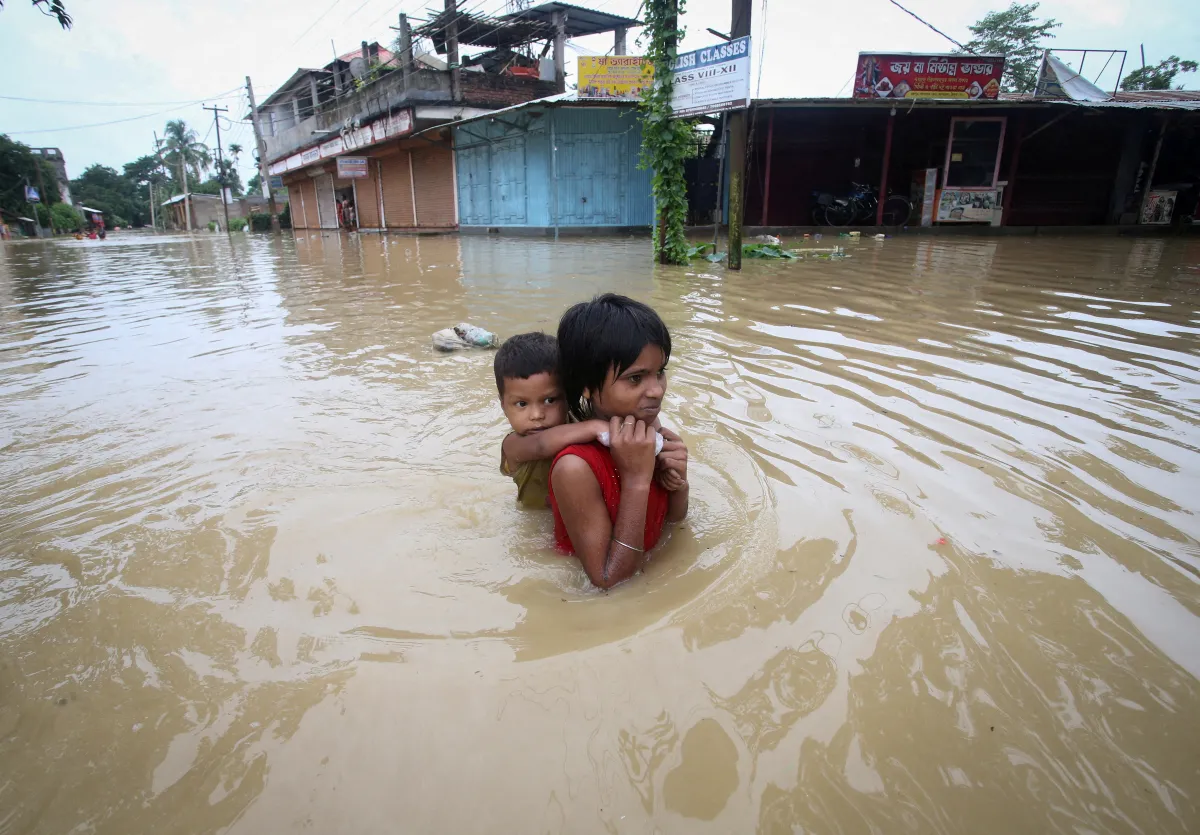 A girl carries her brother as she wades through a flooded road