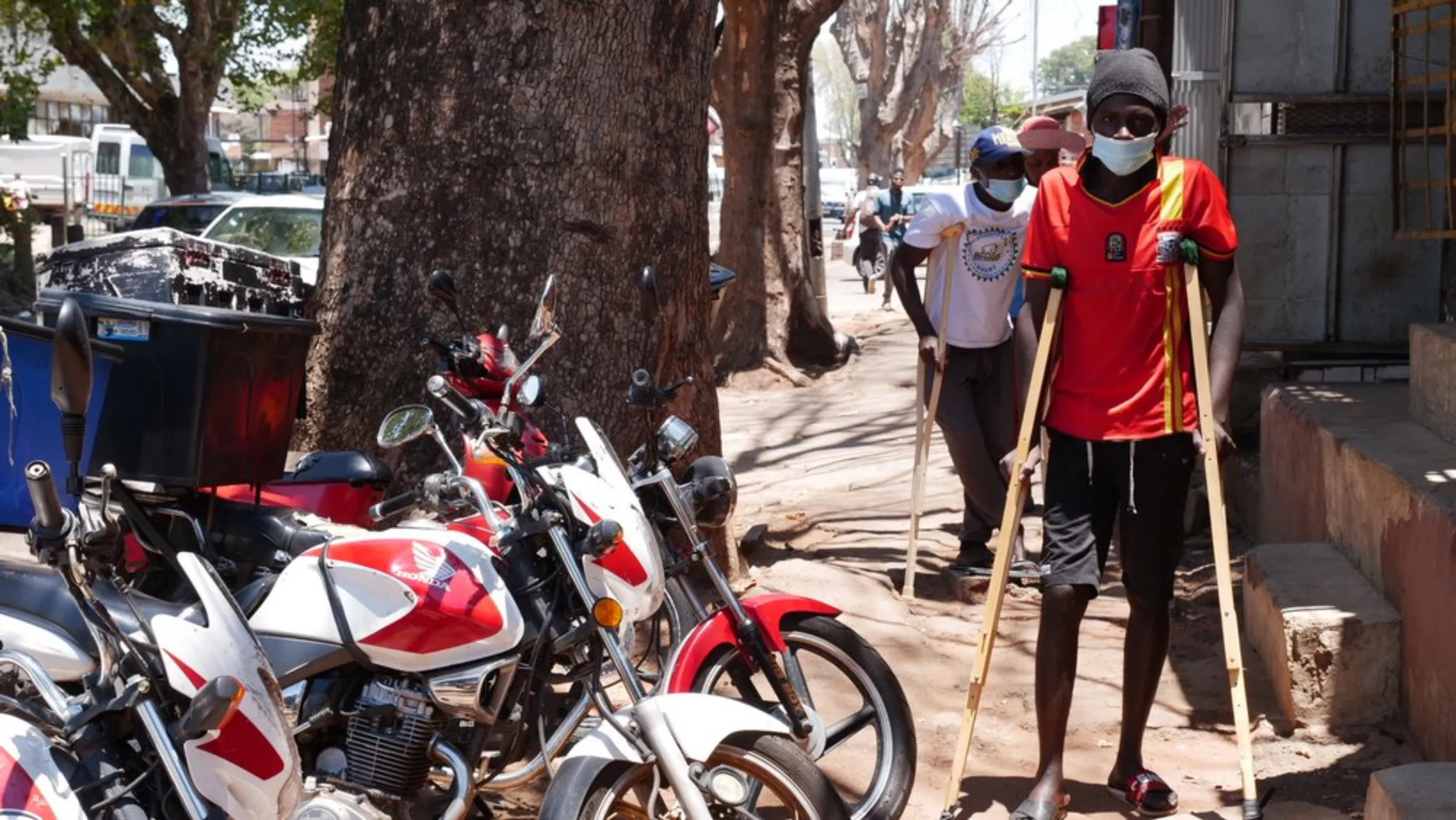 Two food delivery drivers on crutches following recent accidents while driving for Uber Eats pause for a photo alongside motorcycles in Johannesburg, South Africa. January 22, 2021. Thomson Reuters Foundation/Kim Harrisberg