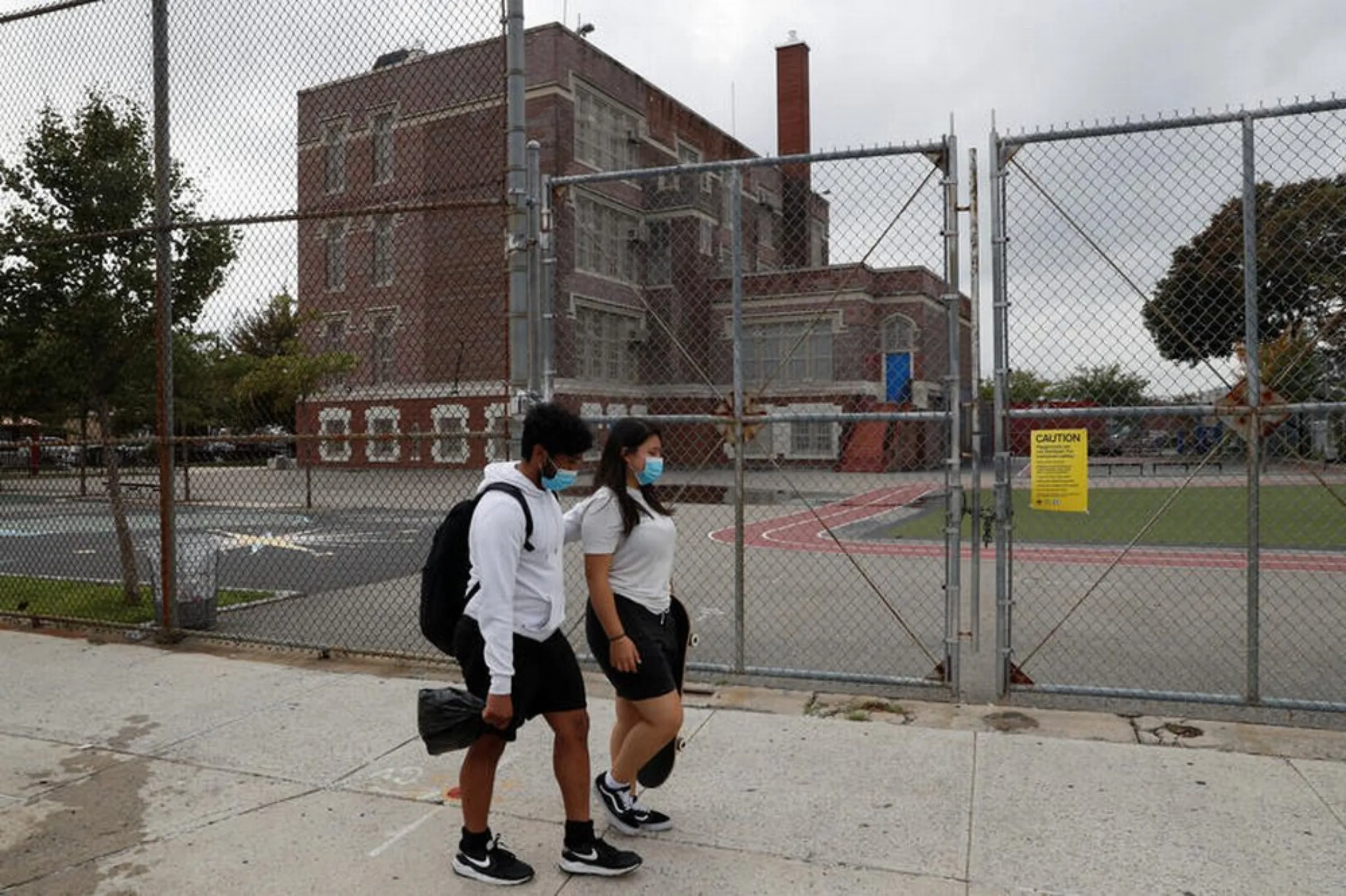 People walk with protective face masks past closed Public School 96 in the Queens borough of New York City, U.S., August 19, 2020