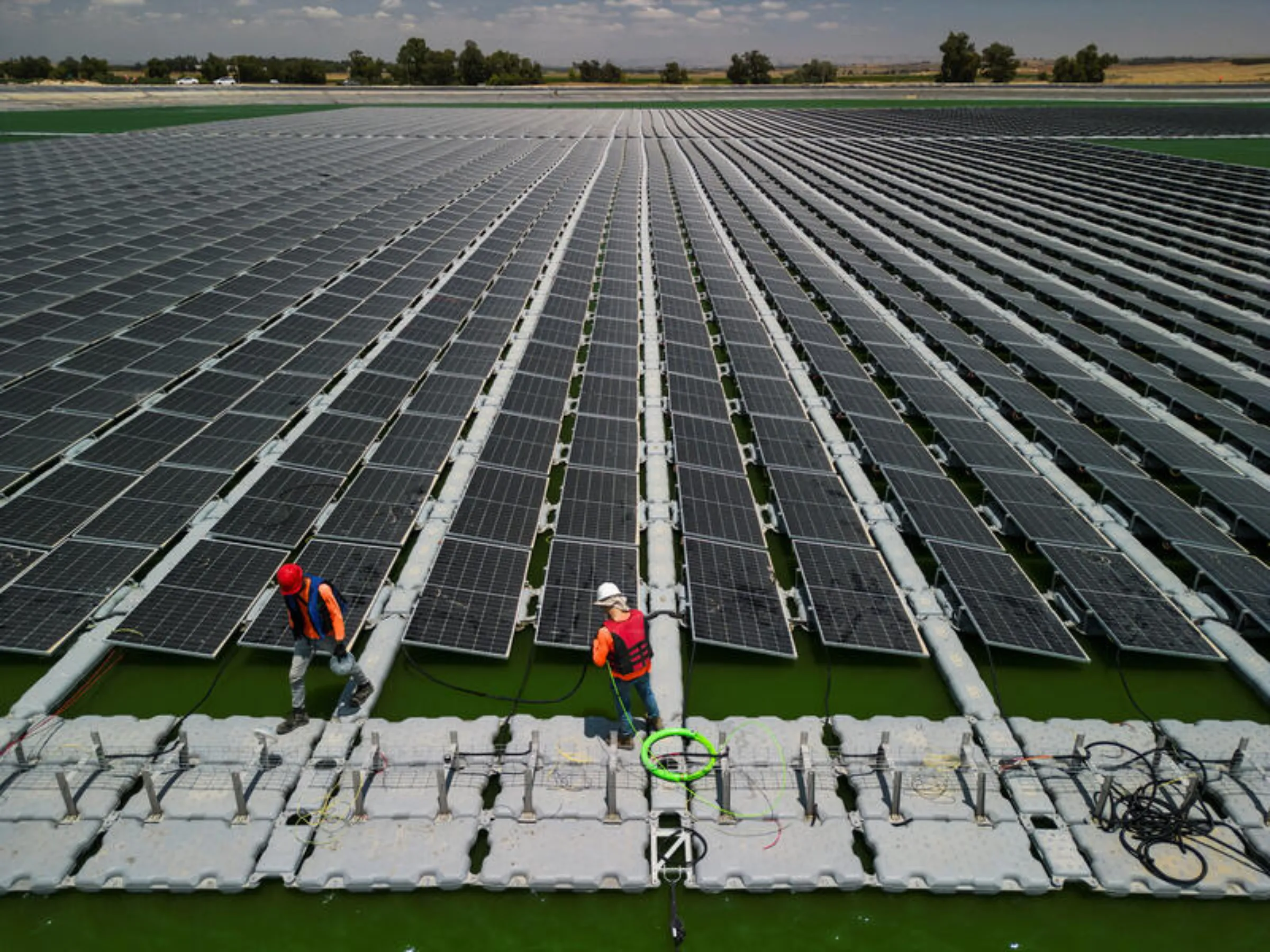 An aerial view shows workers from Nofar Energy installing solar panels on a water reservoir outside of Kibbutz Or HaNer, Israel, June 19, 2023. REUTERS/Amir Cohen