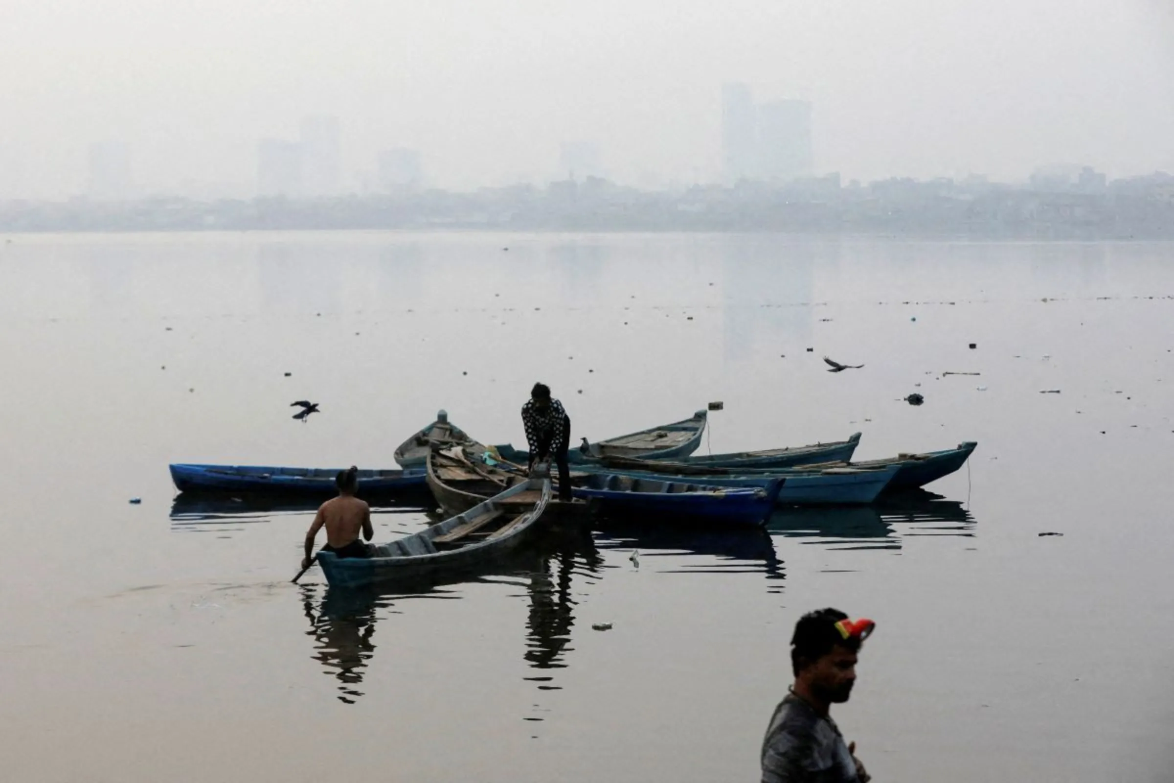 Fishermen are silhouetted as they anchor their boats amid smog, as air pollution levels rise in Karachi, Pakistan November 9, 2023