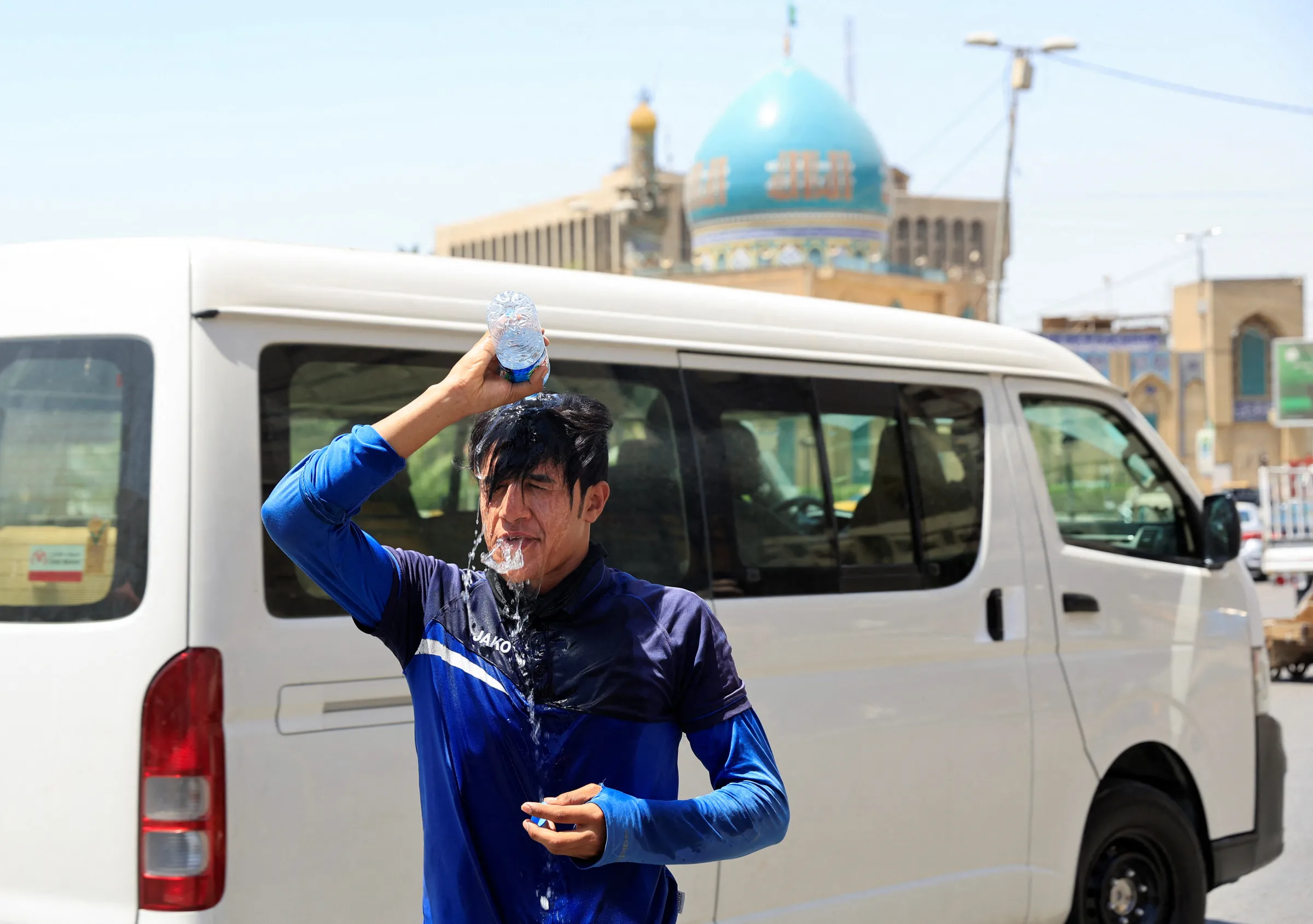 A man pours a bottle of water on his head to cool off at a street during high temperature in Baghdad, Iraq, July 19, 2022. REUTERS/Thaier Al-Sudani