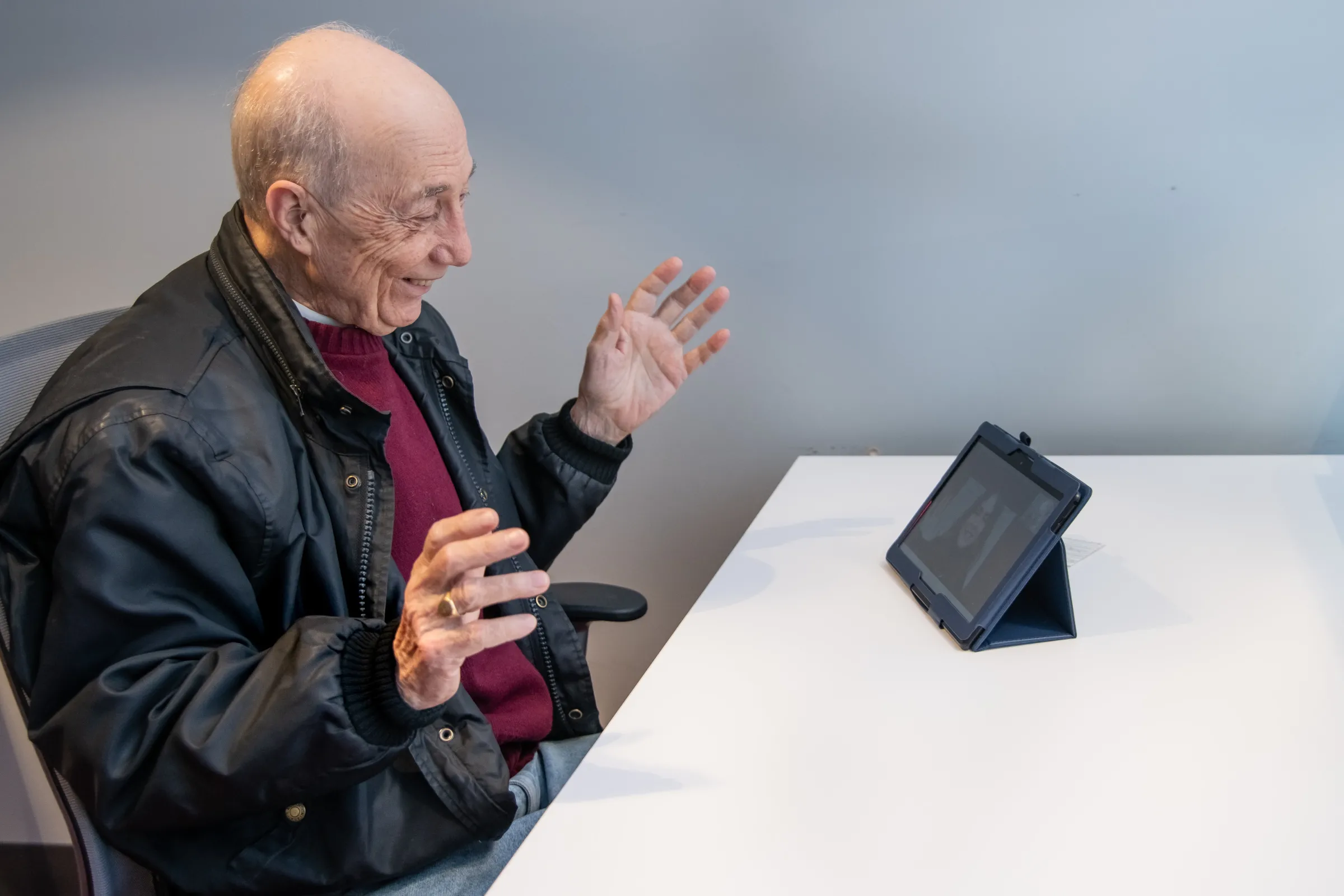 A man sat a desk speaks to someone using a tablet