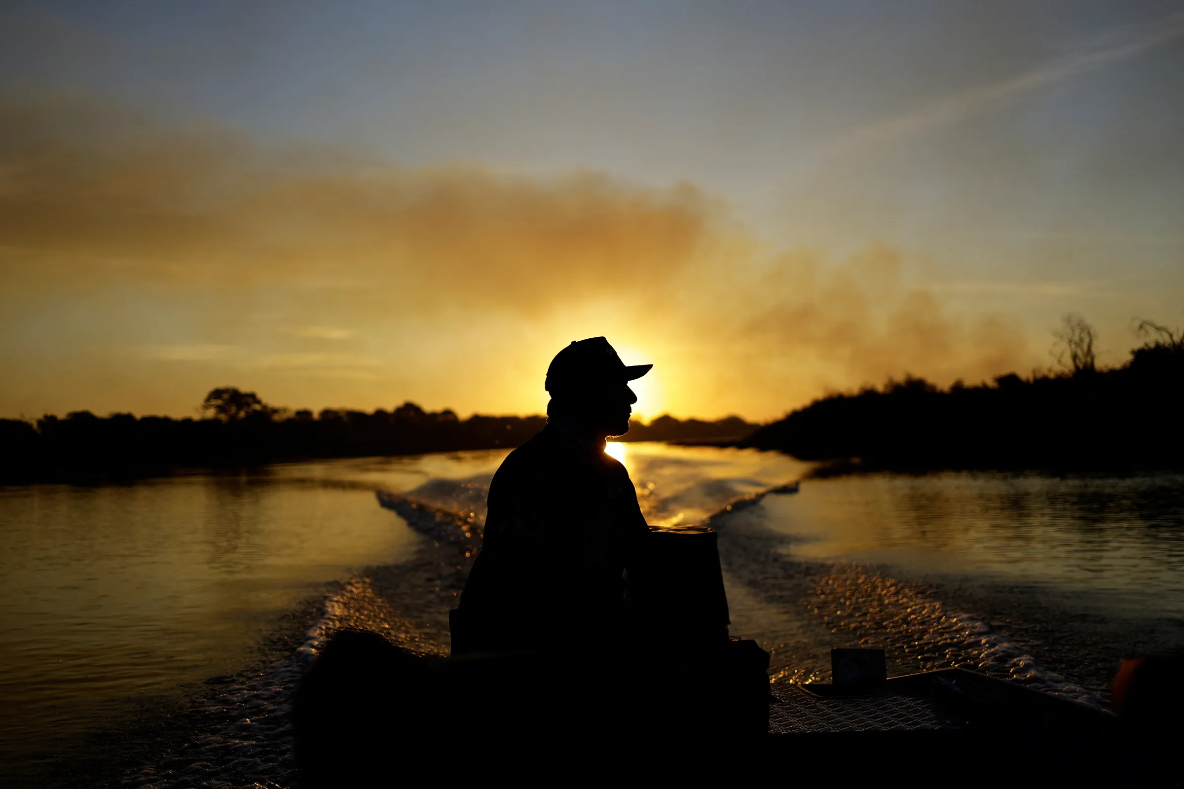 A fisherman sails through the Paraguay River as smoke rises into the air from the fire in the Pantanal, in Corumba, Mato Grosso do Sul state, Brazil, June 11, 2024. REUTERS/Ueslei Marcelino
