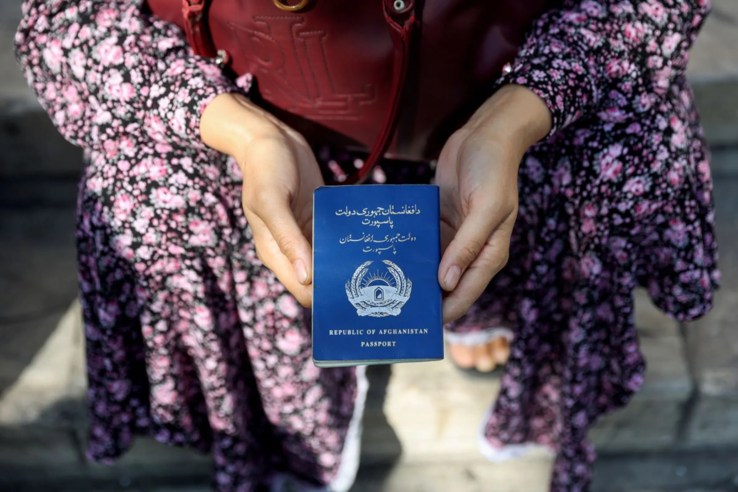 An Afghan refugee holds her passport in front of the German Embassy ​in a bid to acquire refugee visas from the European country, in Tehran, Iran September 1, 2021