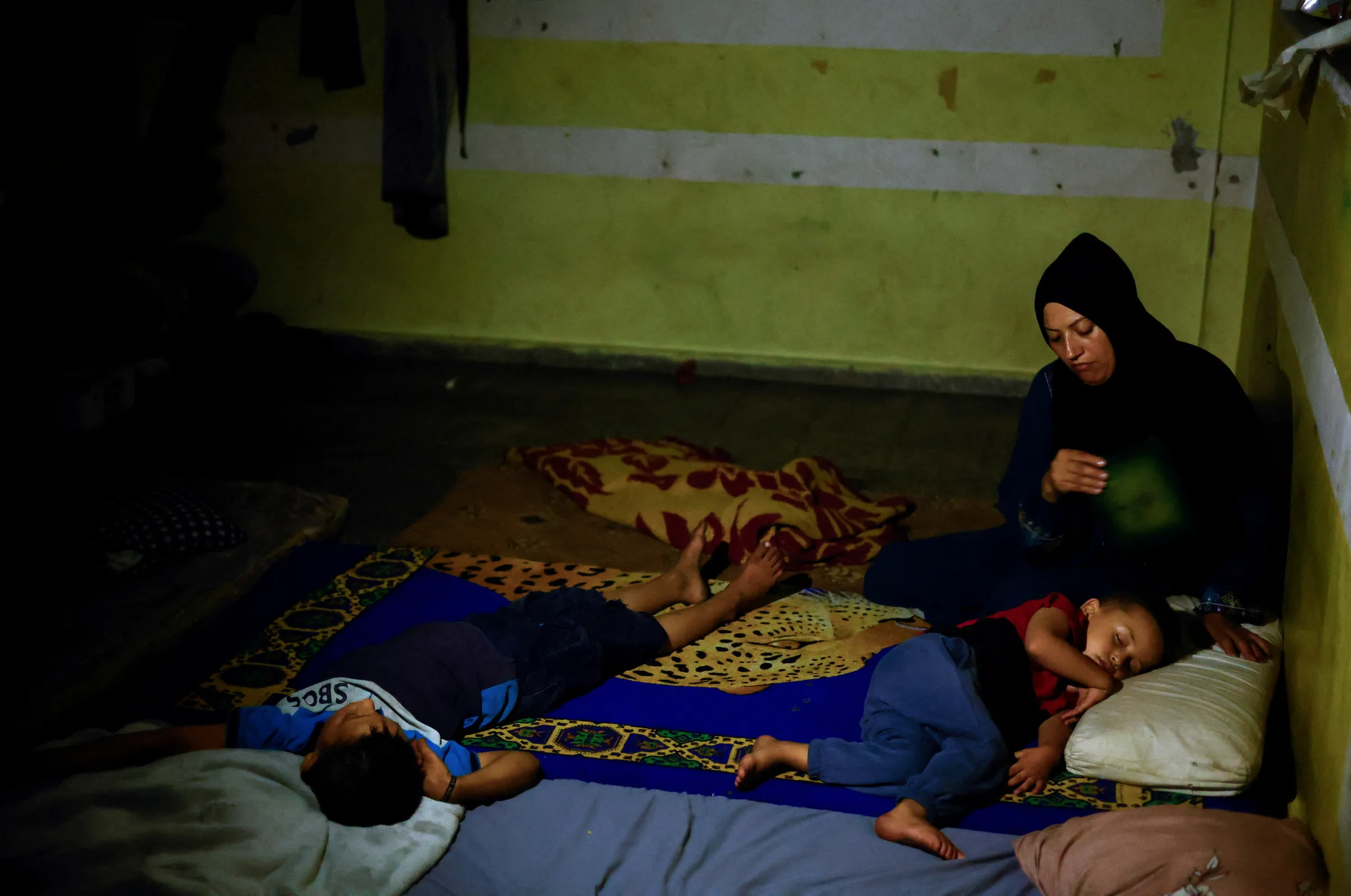 A displaced Palestinian woman fans her children as they sleep in a school where they shelter, during hot weather and power cut, amid Israel-Hamas conflict, in Khan Younis in the southern Gaza Strip, June 25, 2024. REUTERS/Mohammed Salem