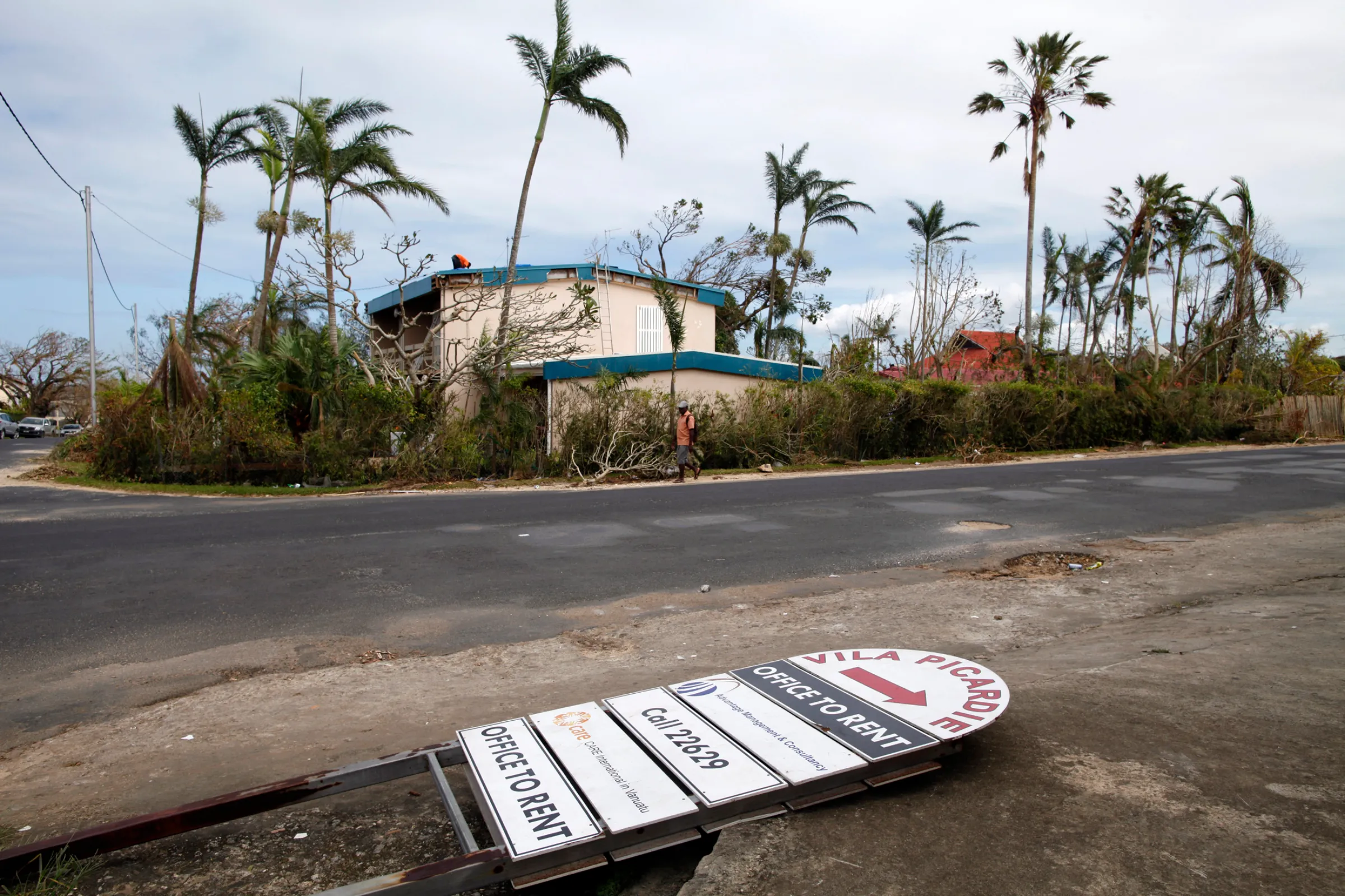 A man passes trees and a fallen shop sign, days after Cyclone Pam in Port Vila