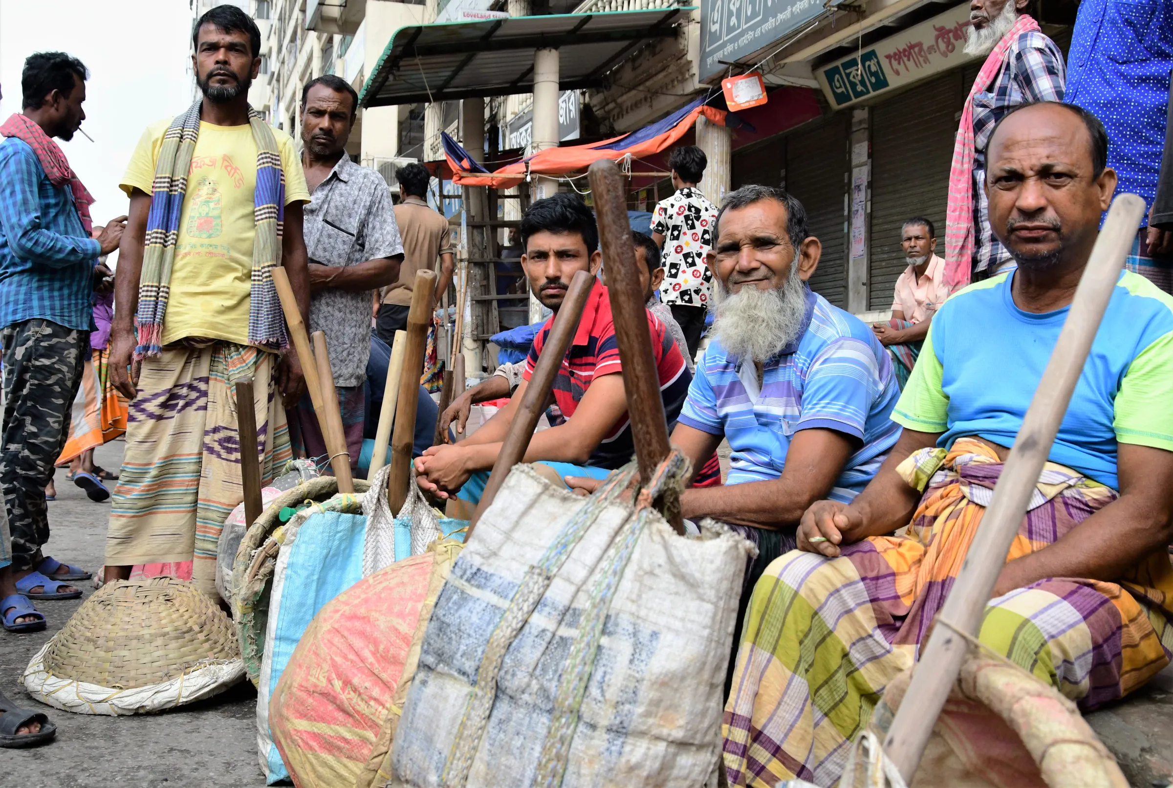 Construction worker Rahim Mia (center, with white beard) sits with other day labourers waiting for work near the Mirpur bridge in Dhaka, Bangladesh, August 16, 2022. Thomson Reuters Foundation/Mosabber Hossain