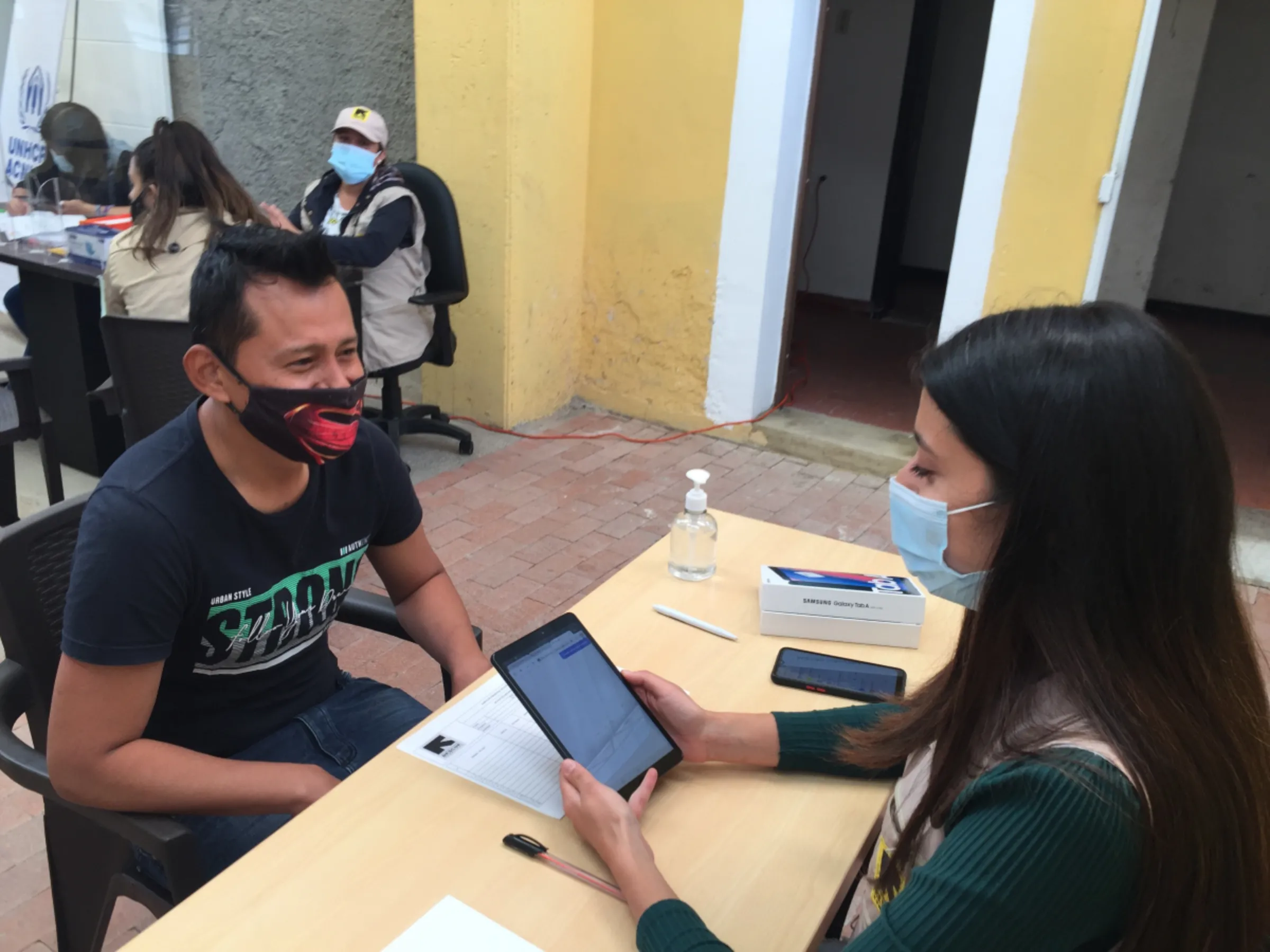 Venezuelan migrant Esneiro Gonzalez receives help from an aid worker with the International Rescue Committee (IRC) to register online for temporary protection status, Soacha, Colombia. July 23, 2021. Thomson Reuters Foundation/Anastasia Moloney