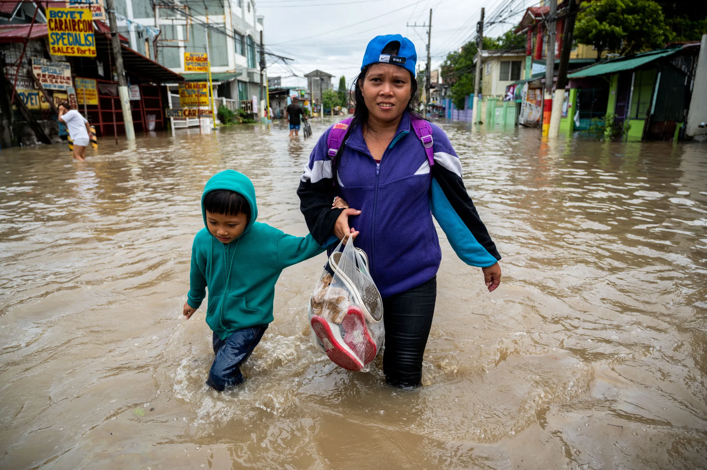A mother and a child wade through a flooded street following heavy rains brought by Tropical Storm Nalgae, in Kawit, Cavite province, Philippines, October 30, 2022