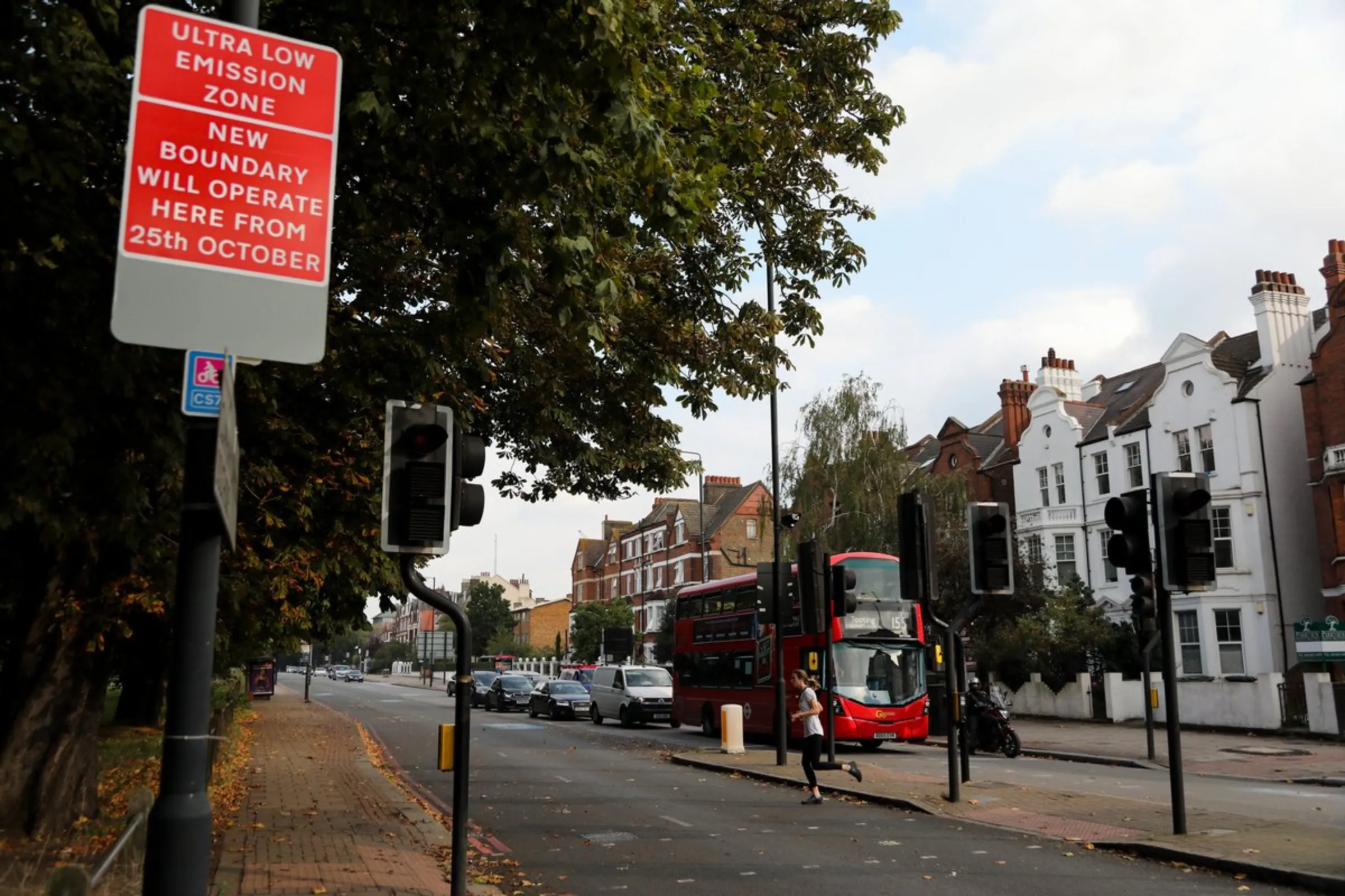 A jogger crosses the road near a London double-decker bus and a sign advising motorists of the expansion of London’s Ultra Low Emissions Zone (ULEZ), aimed at cleaning the city’s air, on October 19, 2021