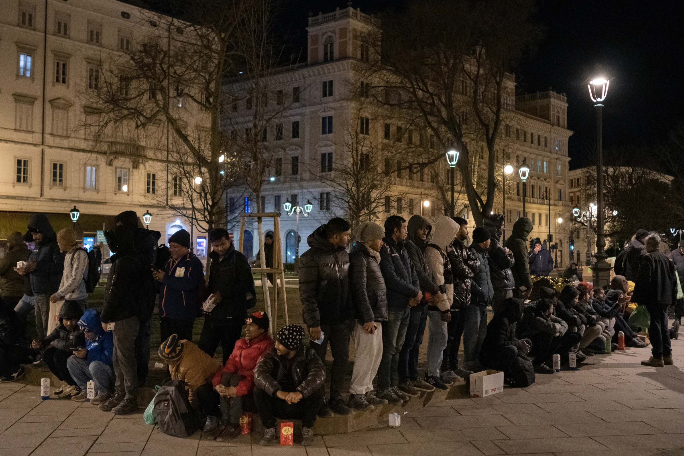 People on the move line up to receive emergency support and food  from the International Rescue Committee's outreach team in the Piazza della Liberta, opposite Trieste Centrale railway station, in Trieste, Italy. March 4, 2024. Francesco Pistilli/International Rescue Committee/Handout via Thomson Reuters Foundation