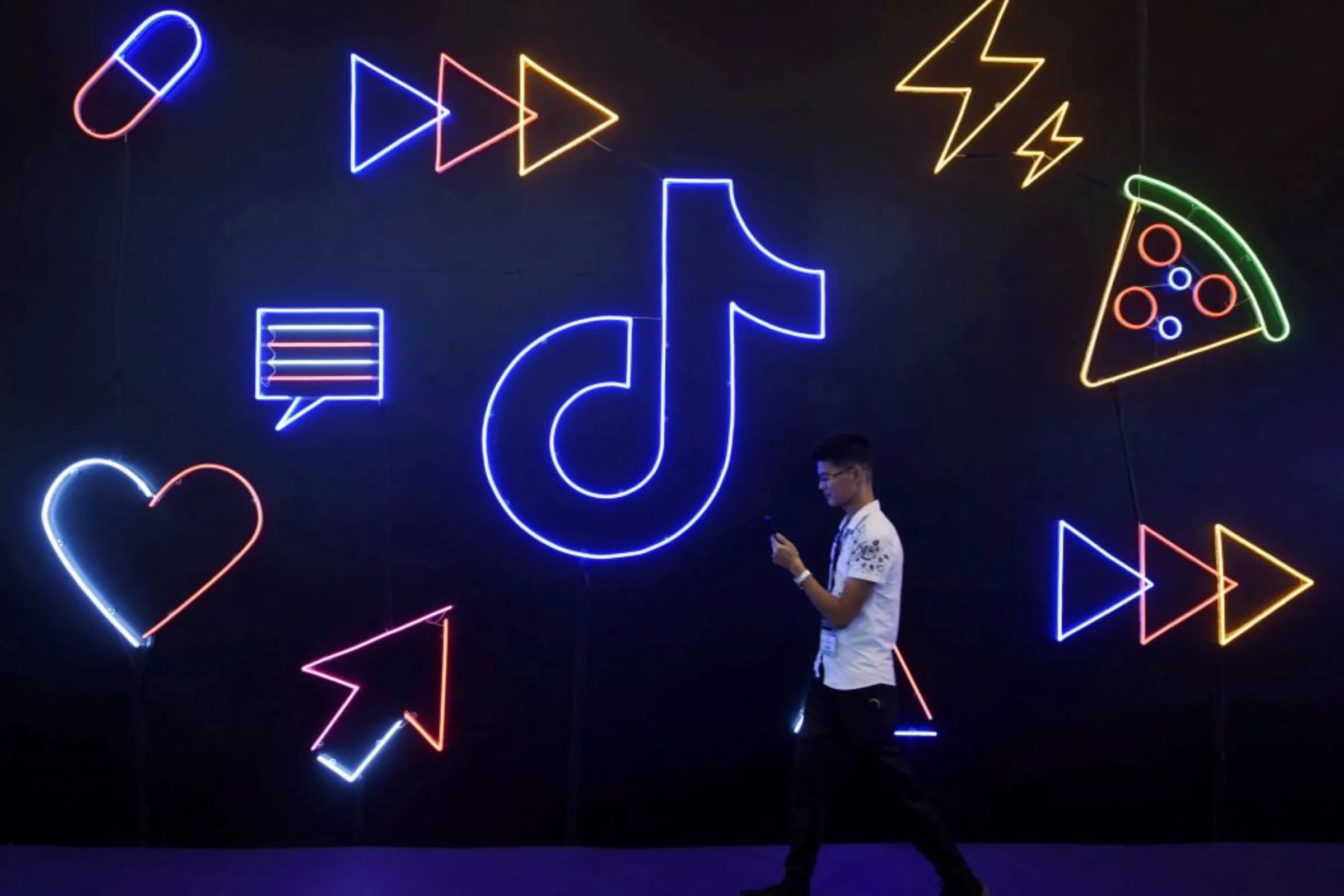 A man holding a phone walks past a sign of Chinese company ByteDance's app TikTok, known locally as Douyin, at the International Artificial Products Expo in Hangzhou, Zhejiang province, China October 18, 2019